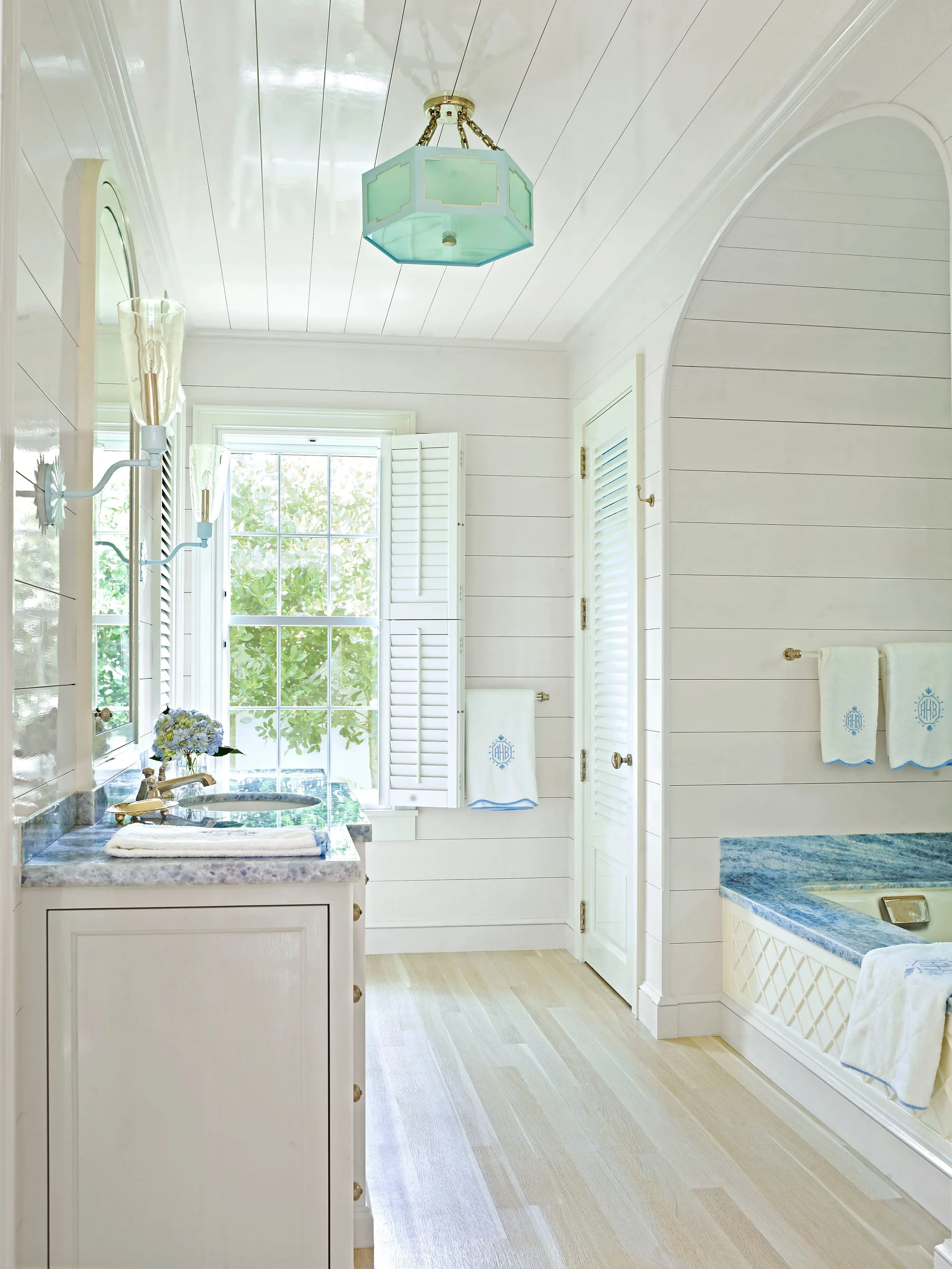 Bright white shiplap bathroom featuring a blue marble vanity countertop, a matching built-in tub surround, and light wood floors.