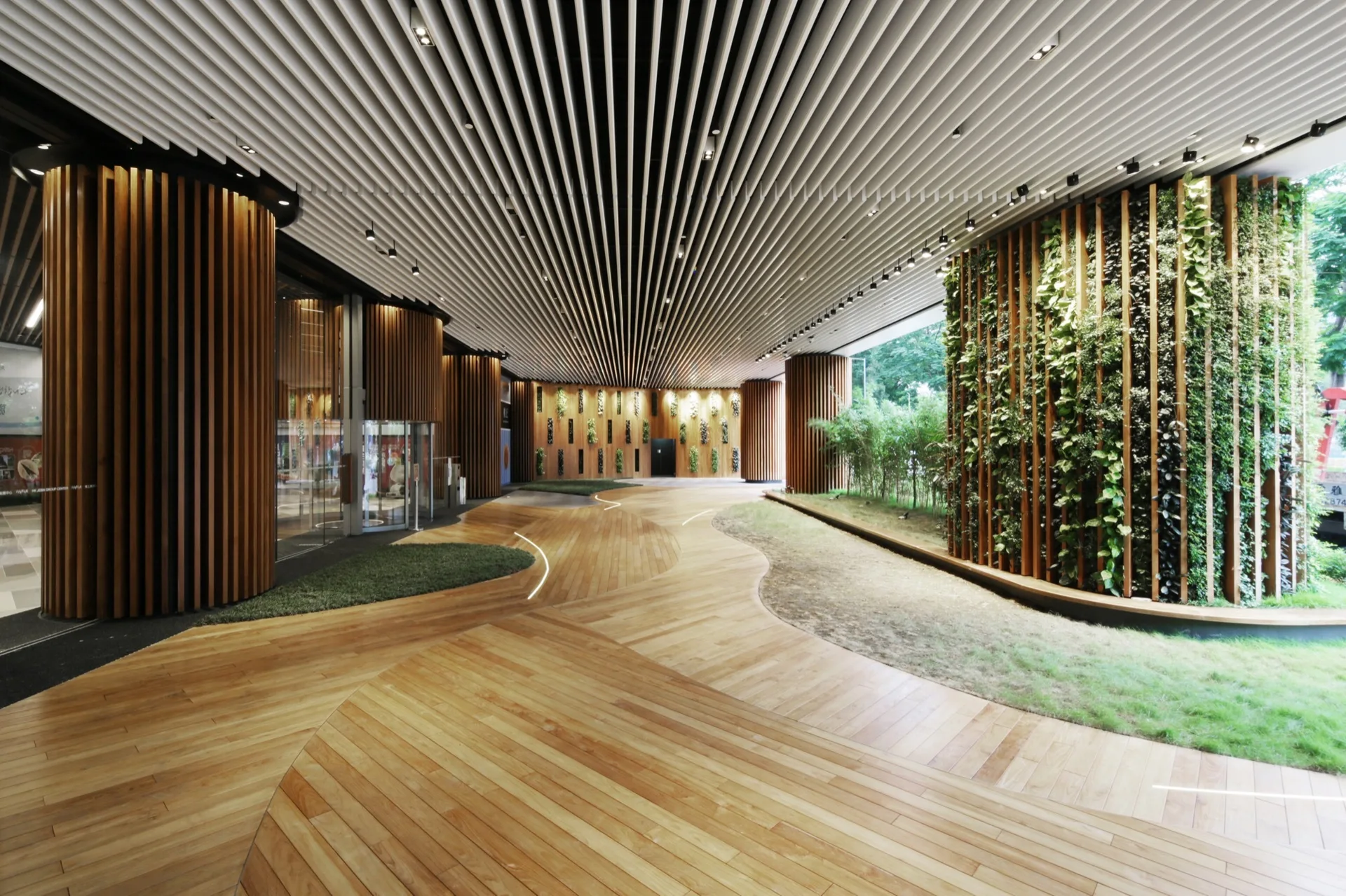 A spacious modern lobby features a white baffle ceiling, curved wooden plank flooring, wood-slat columns, and integrated vertical gardens.