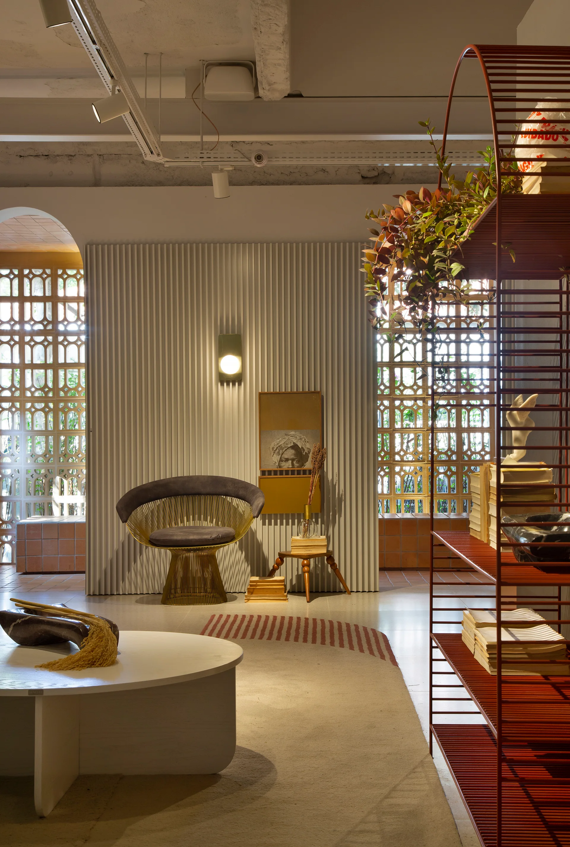 A contemporary lounge featuring a gold wire-frame armchair, a white fluted wall panel, and a terracotta-colored breeze block partition.