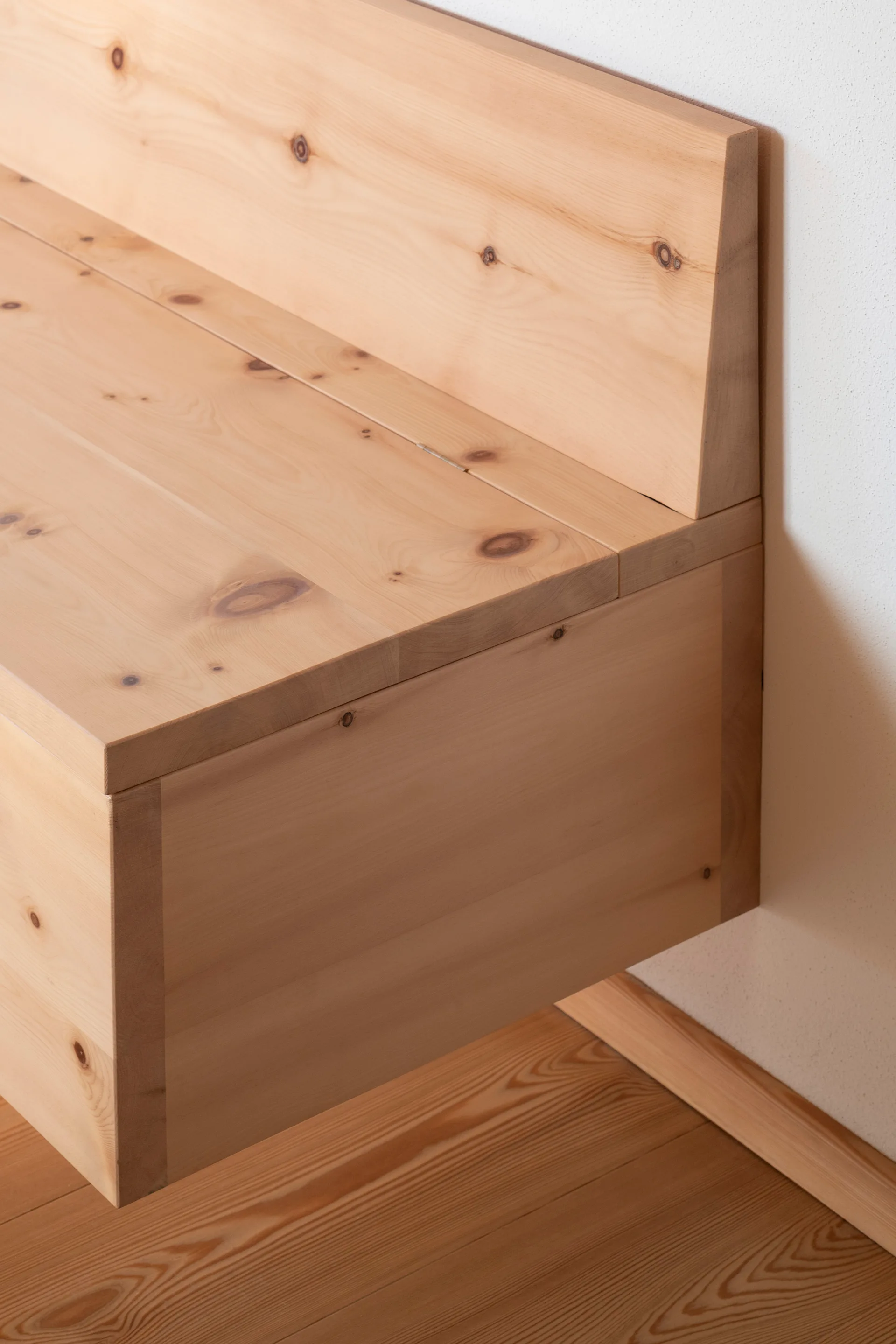 A minimalist light wood floating bench with visible knots is mounted to a white wall above a matching light wood floor.