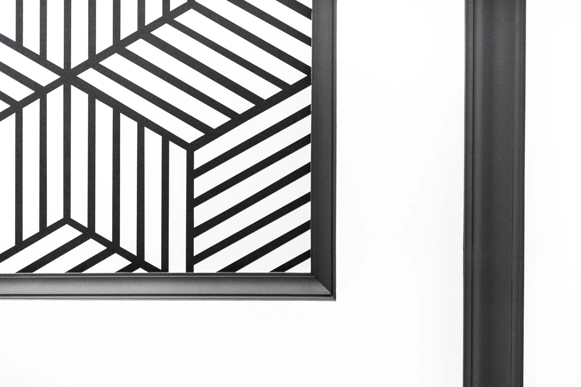 A close-up of a black-framed geometric art print with a cube pattern hanging on a white wall next to a vertical black trim piece.