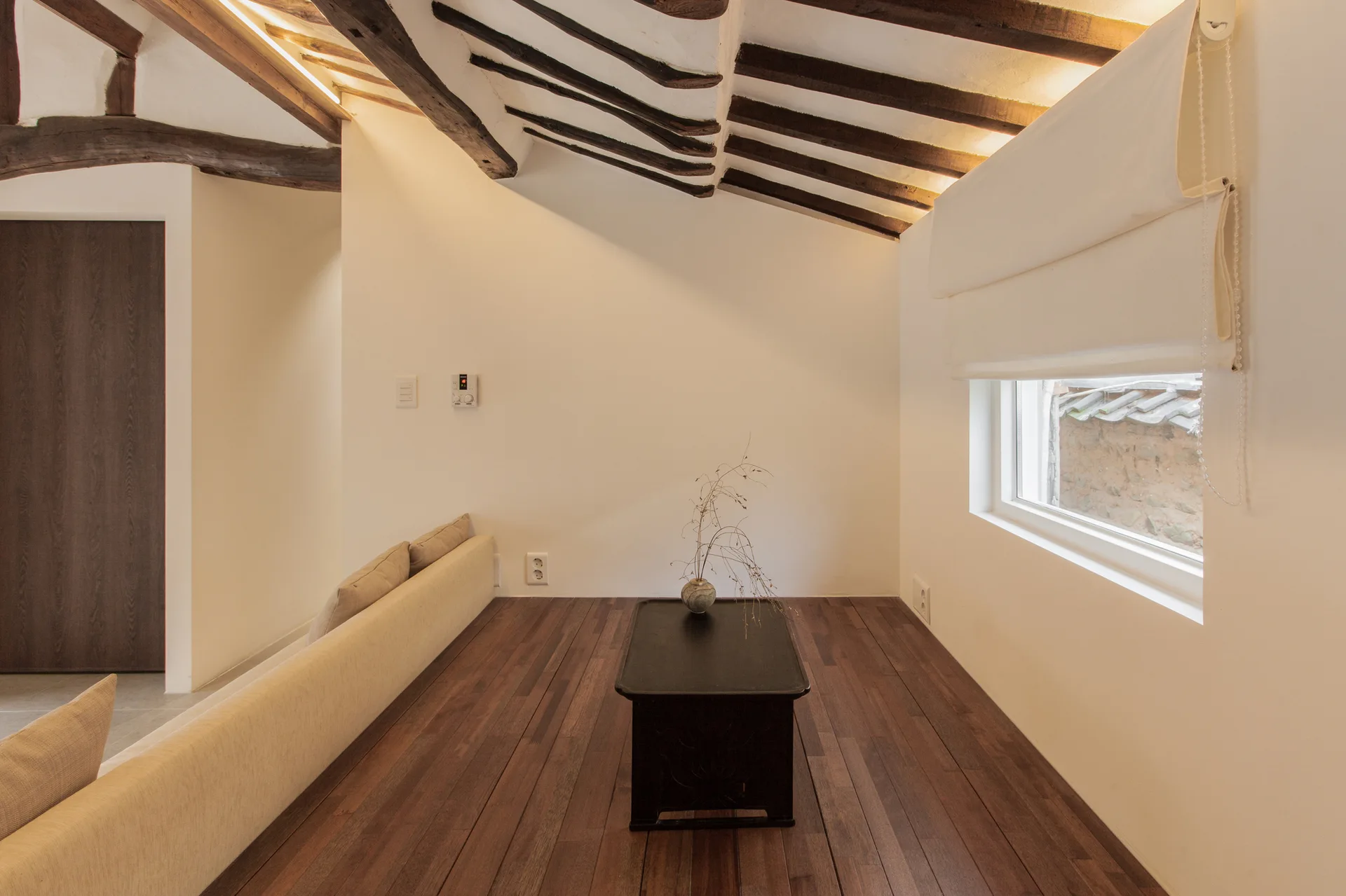 A minimalist living space with a low black coffee table on dark wood floors under a slanted ceiling with exposed wooden rafters.