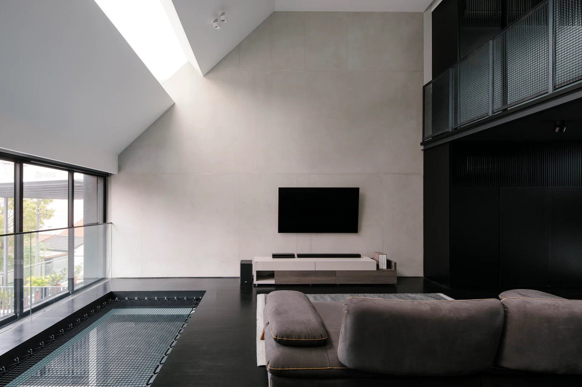 A modern loft living room featuring a concrete-paneled accent wall, a gray sofa, and a black mesh hammock net integrated into the floor.