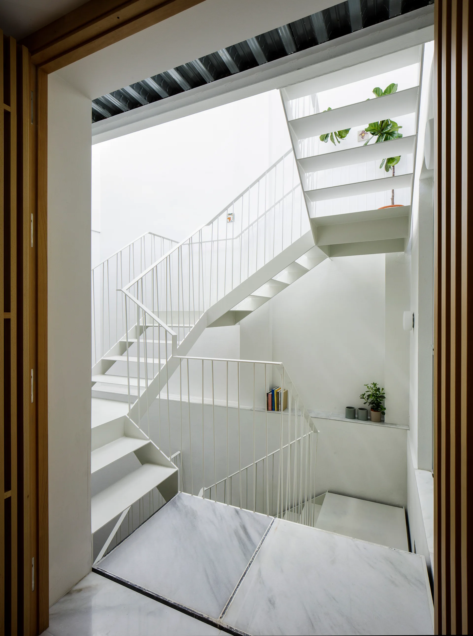 A minimalist white metal staircase with open treads and vertical railings rises from a polished grey-veined marble landing.