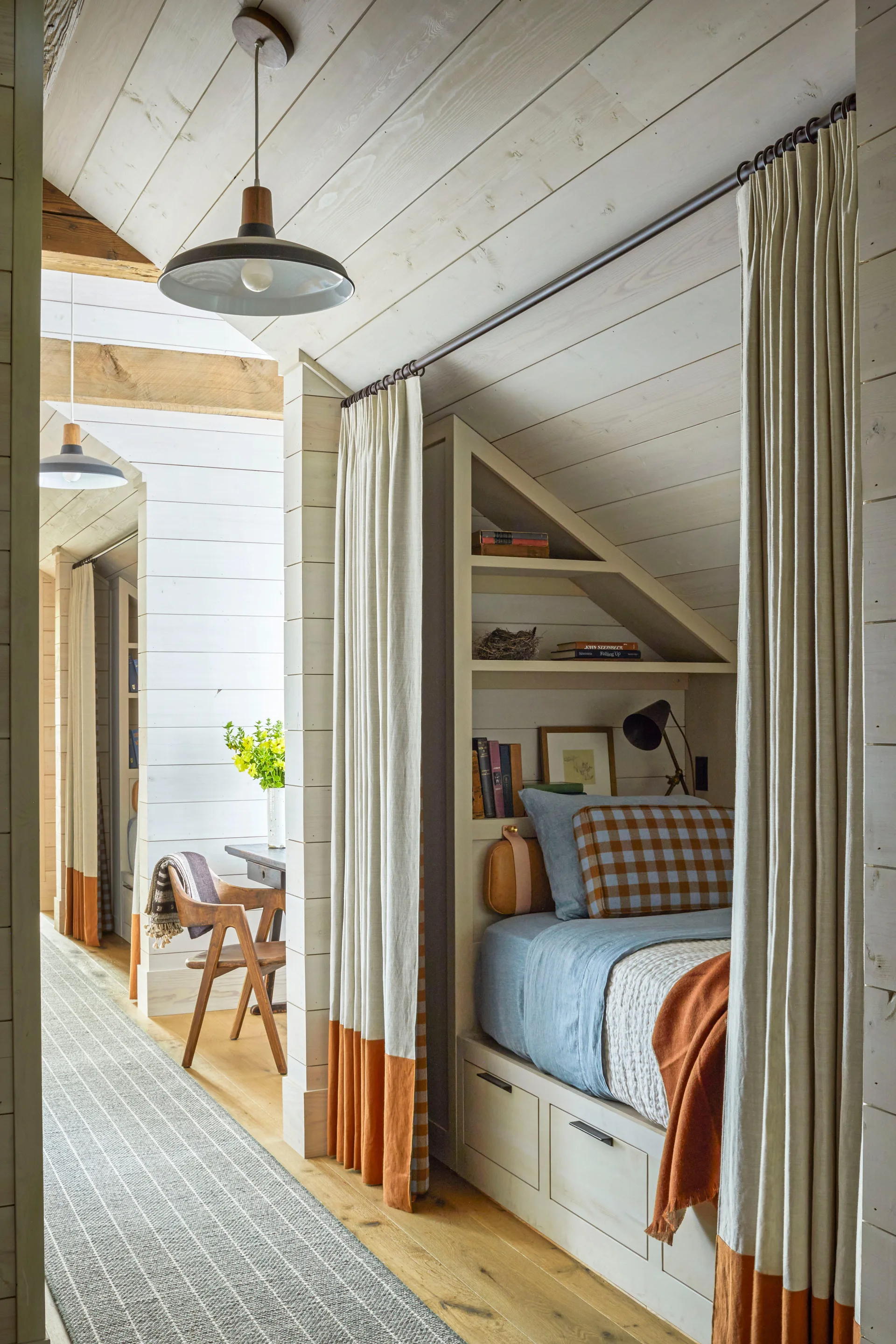 A built-in wooden sleeping nook features integrated shelving, under-bed storage drawers, and cream curtains with a terracotta bottom band.
