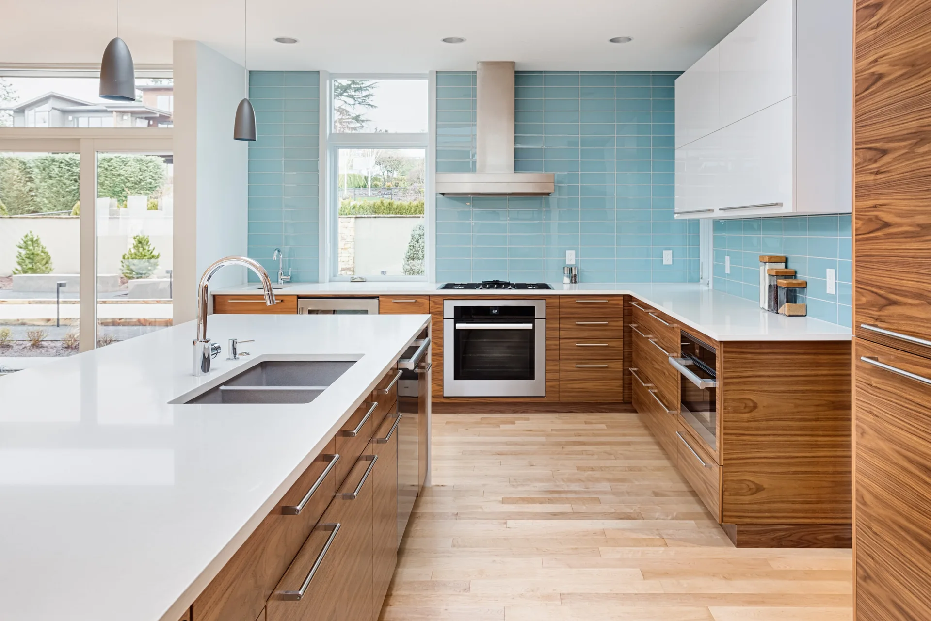 A modern residential kitchen featuring wood-toned base cabinets, a light blue subway tile backsplash, white upper cabinets, and a central kitchen island.