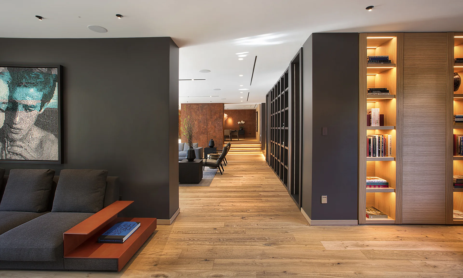 A modern home interior with dark charcoal walls, light wood flooring, and an oak bookcase built into the wall with warm interior lighting.