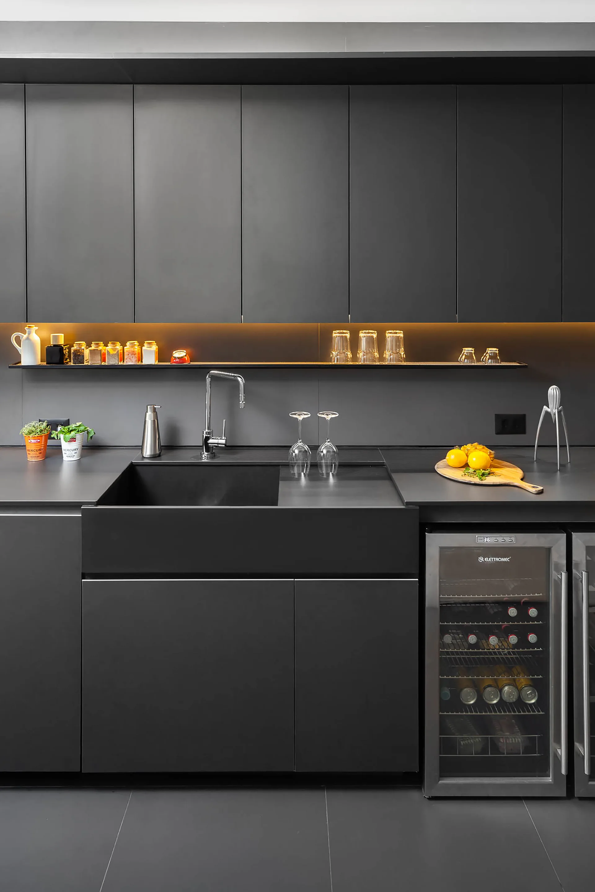A modern kitchen featuring matte black cabinets, an integrated sink, an under-cabinet illuminated shelf, and a built-in wine fridge.