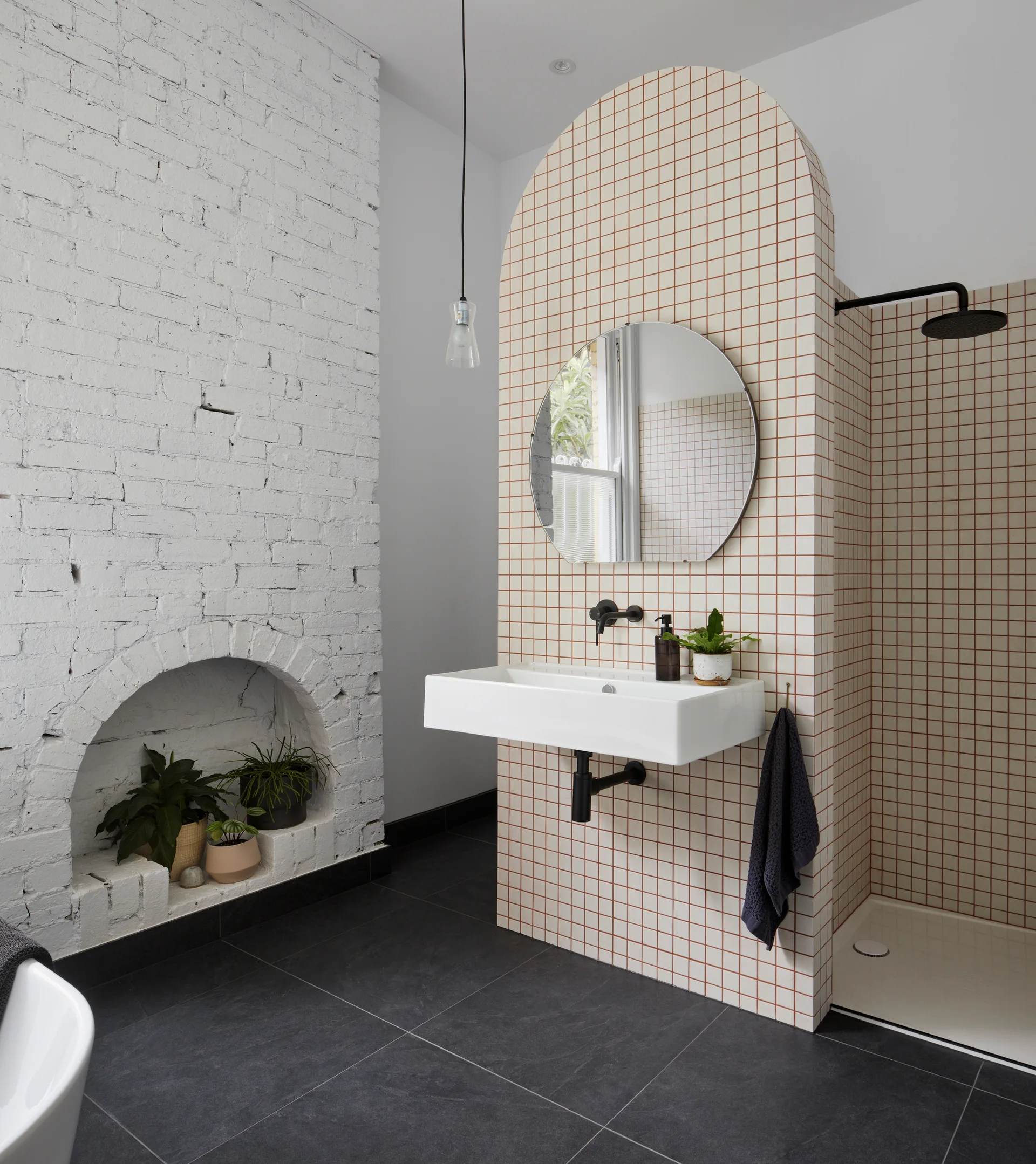 A modern bathroom features a white grid-tiled arched partition, a floating sink, and a painted white brick wall with a hearth.