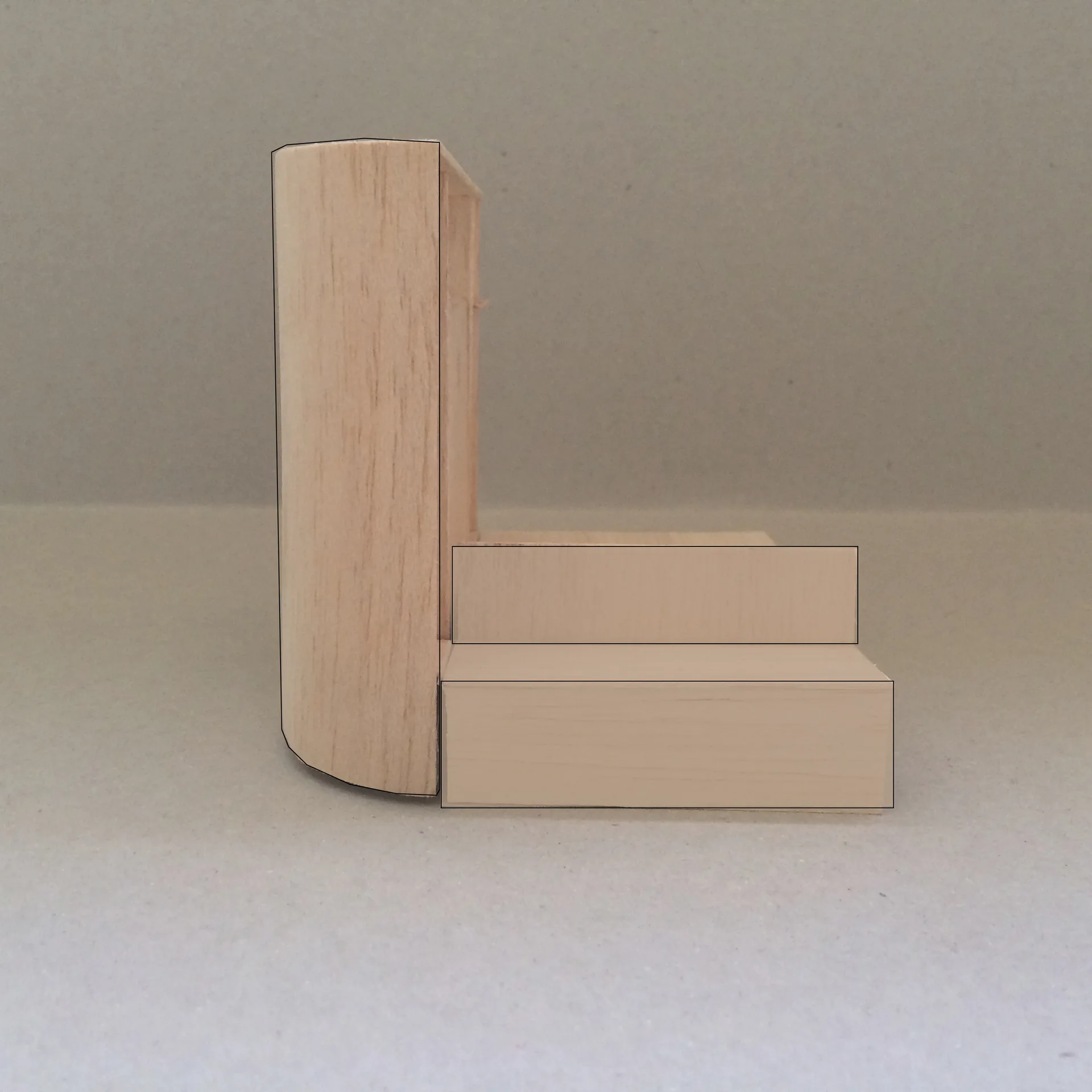 A miniature wooden architectural model showing a small set of light wood steps next to a curved vertical wall against a plain gray background.