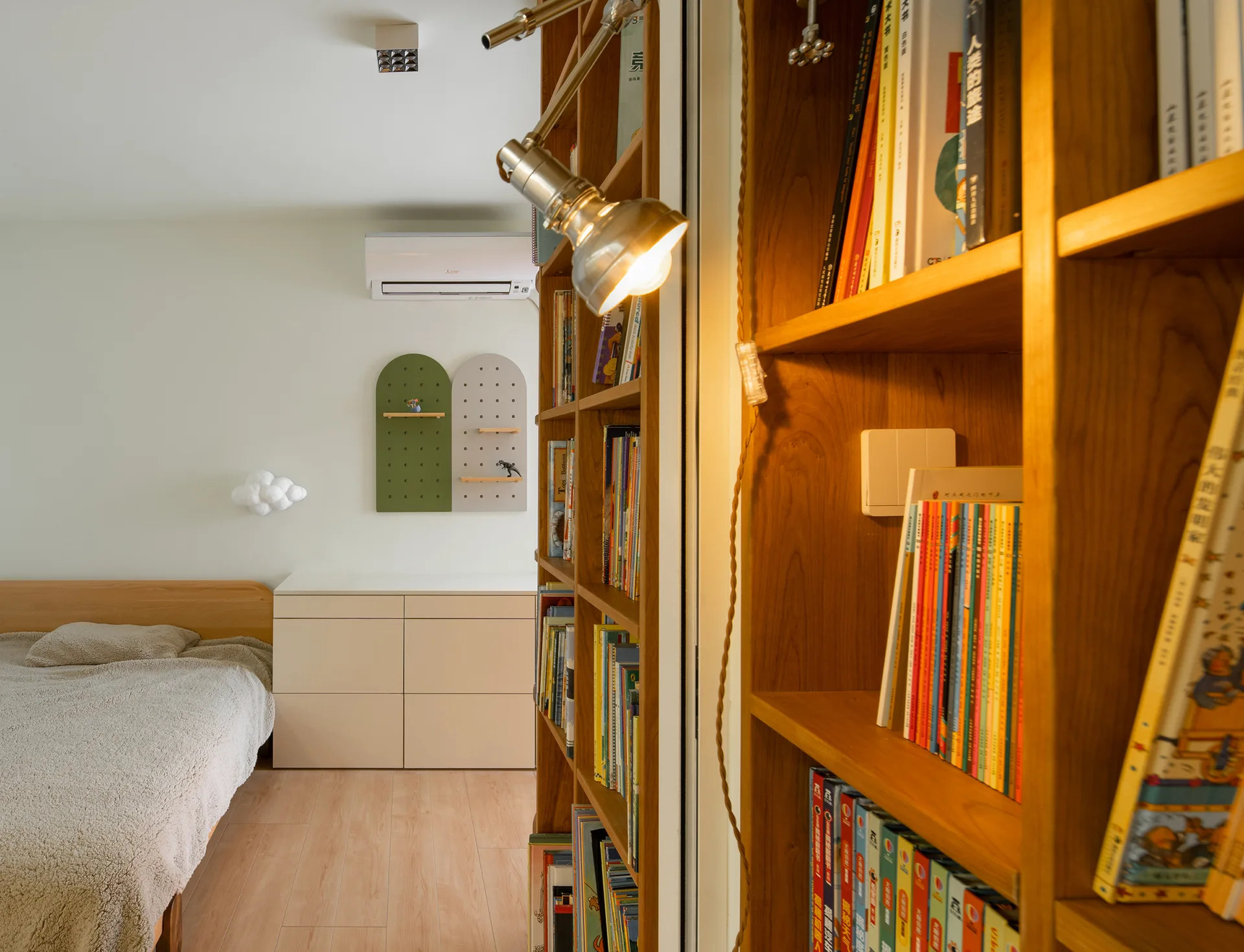 A bedroom featuring a tall wooden bookshelf, a cozy bed, a minimalist dresser, and two arched pegboards mounted on the wall.