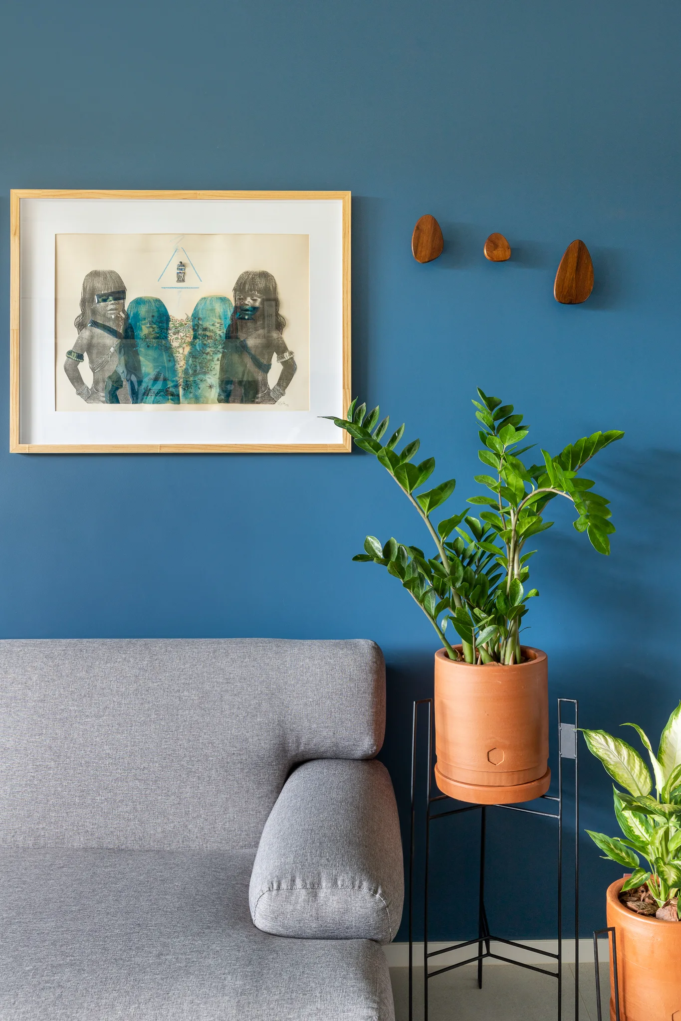 A grey upholstered sofa sits against a deep blue painted wall next to a ZZ plant in a terracotta pot on a black metal stand.