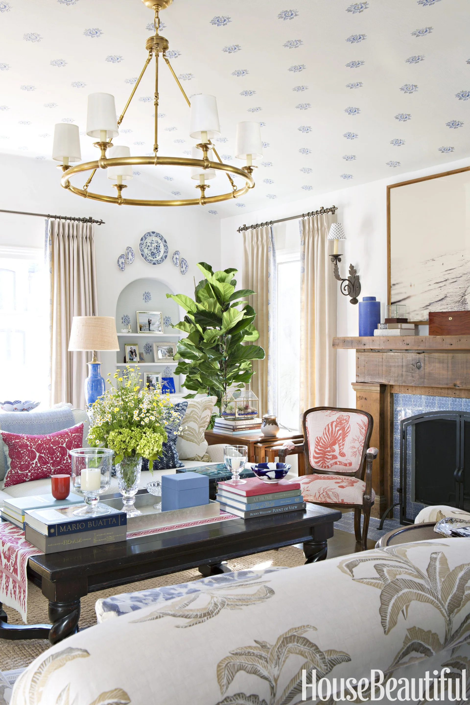 A classic living room features a blue patterned ceiling, a brass chandelier, a dark wood coffee table, and a fireplace with blue tile surround.