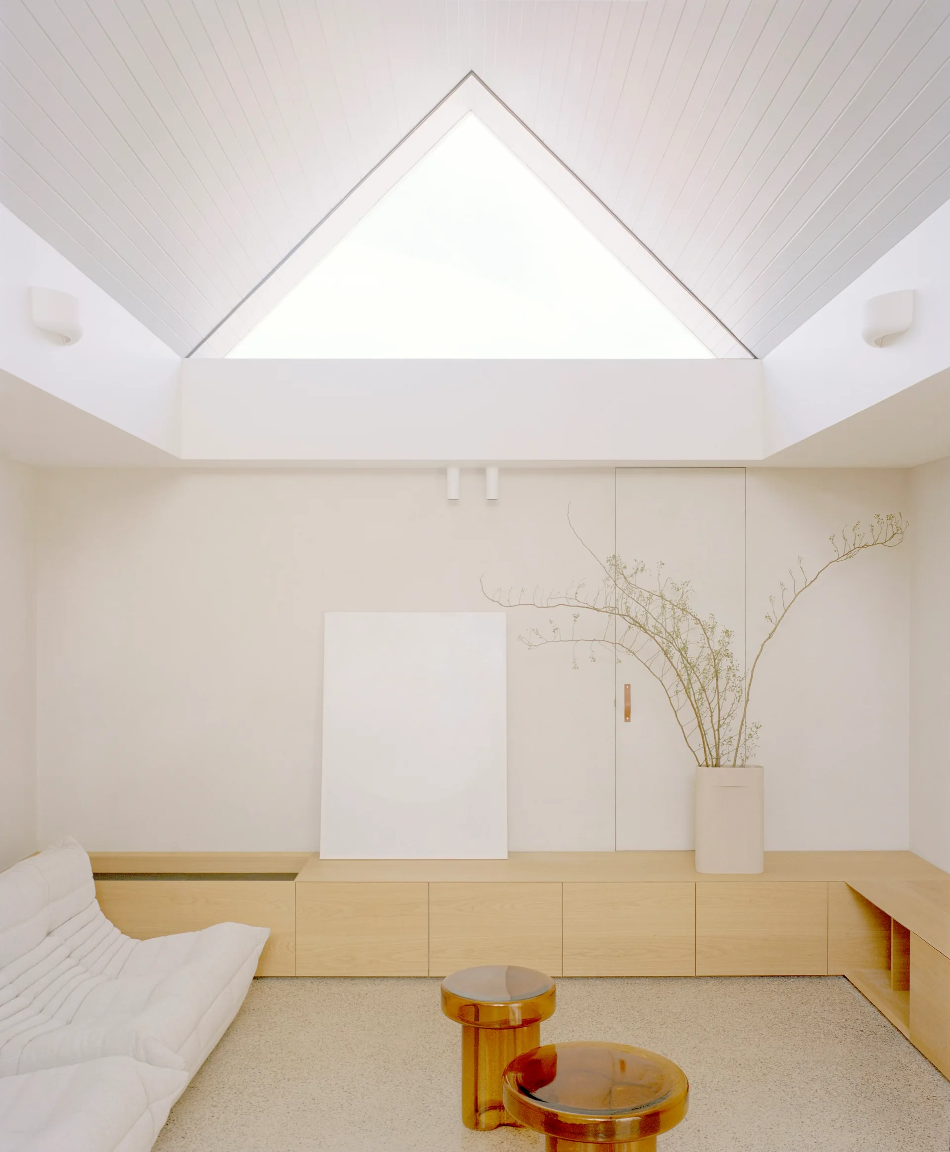 A minimalist living room features a triangular skylight set into a gabled ceiling, a low-profile white sofa, and a long light wood credenza.