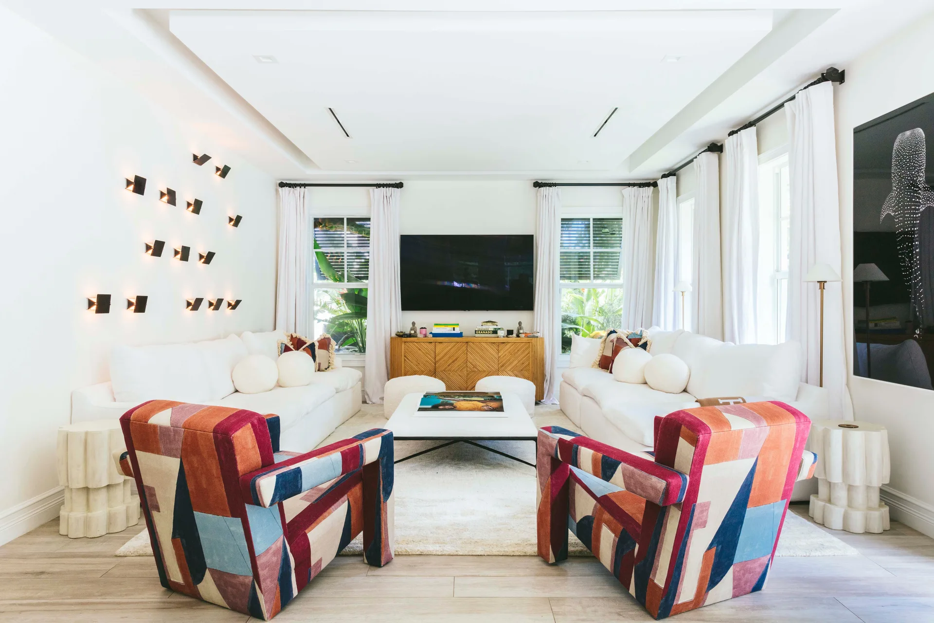 A symmetrical living room featuring two white sofas, a pair of colorful geometric patterned armchairs, and a wall of illuminated sconces.