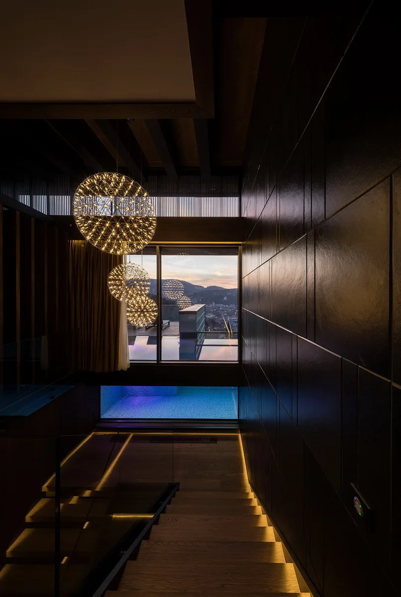 A modern wooden staircase with under-step LED lighting is flanked by a dark paneled wall, with three glowing spherical pendant lights hanging above.