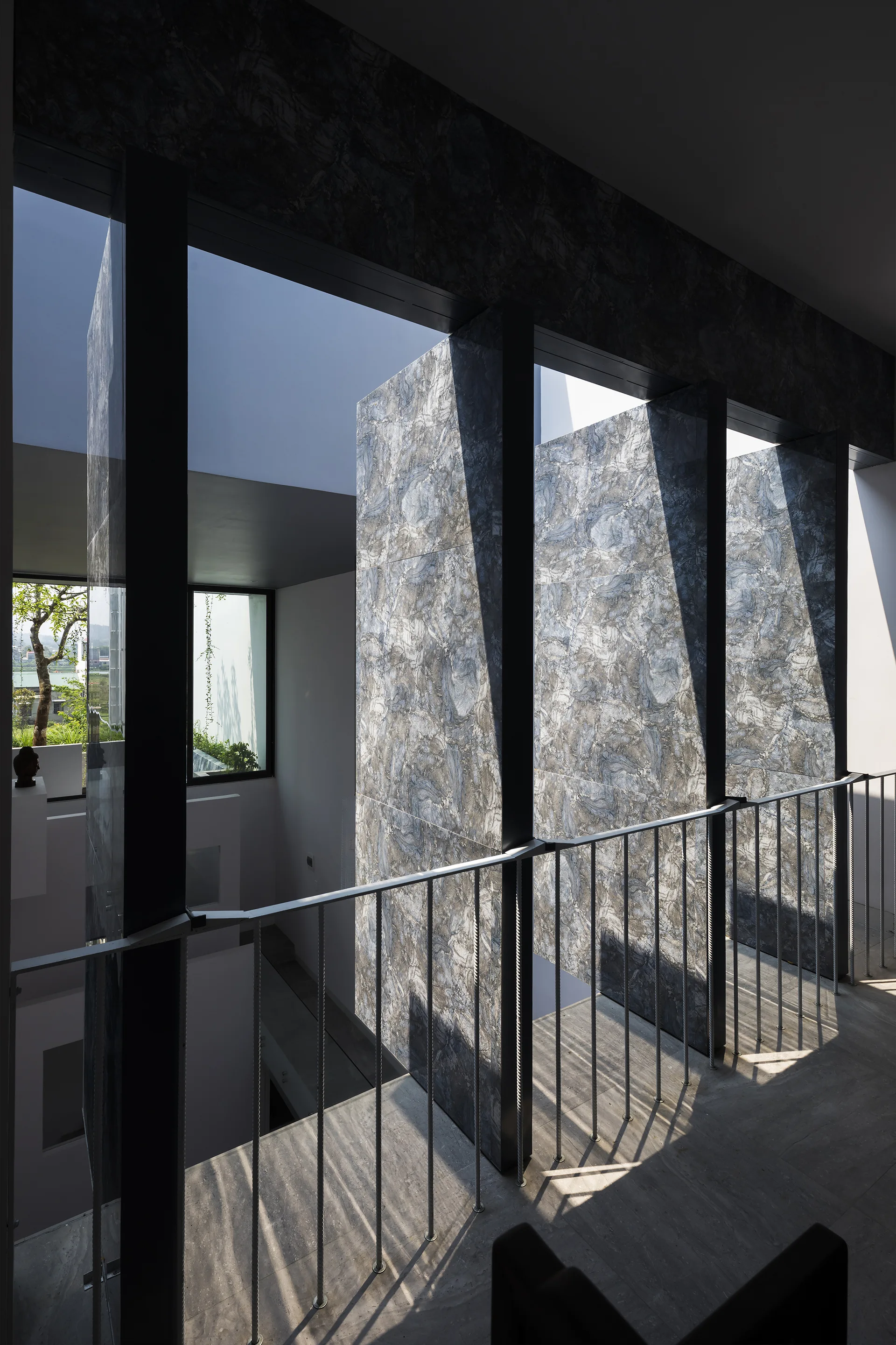 A modern interior landing features tall vertical marble-patterned partition walls and a metal handrail casting shadows on the stone floor.