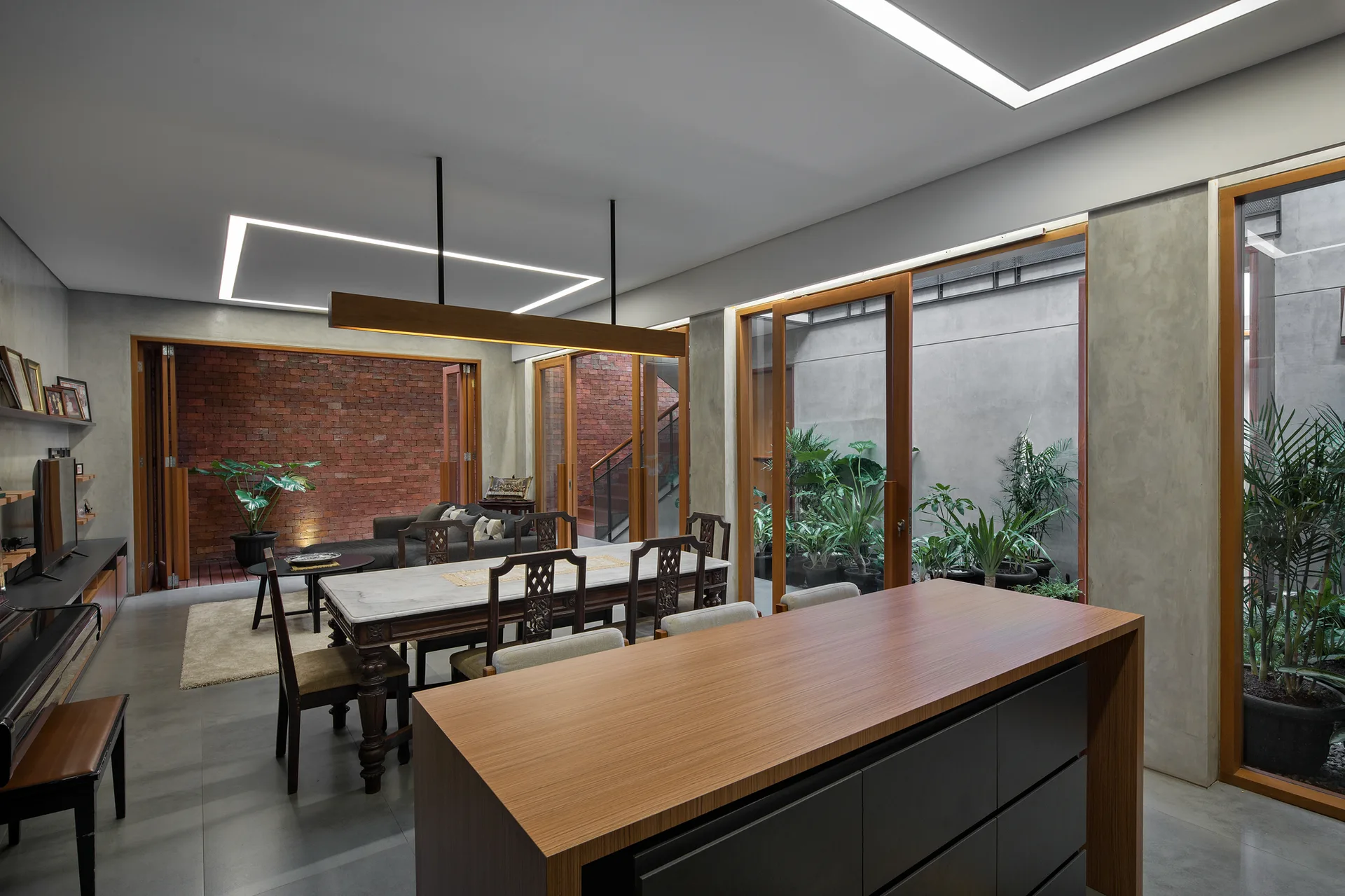 An open-concept dining room features a marble-topped table, a wood island, polished concrete floors, and sliding glass doors opening to a courtyard.