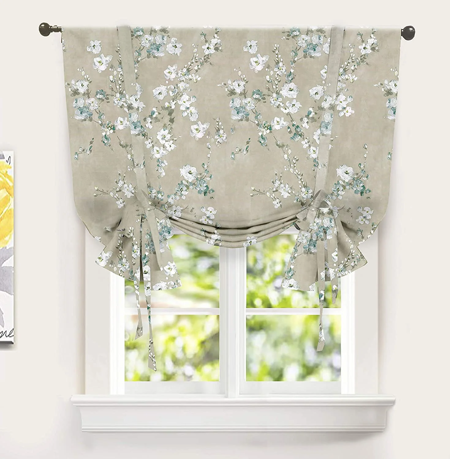 A beige tie-up window shade with a white and sage green floral pattern hangs on a black curtain rod over a white window.