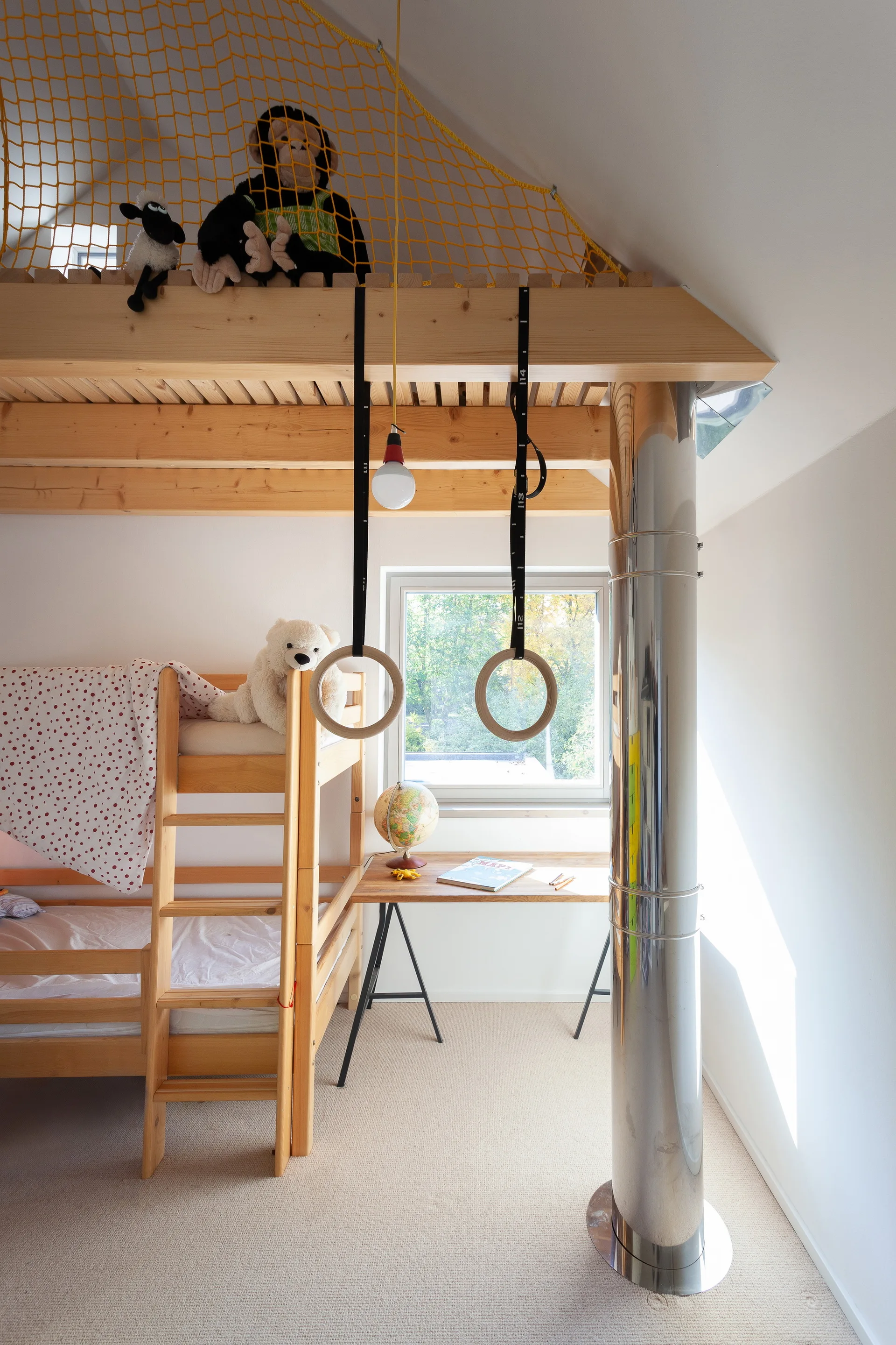 A child's bedroom features a wooden bunk bed, a small desk by the window, suspended gymnastics rings, and yellow overhead safety netting.