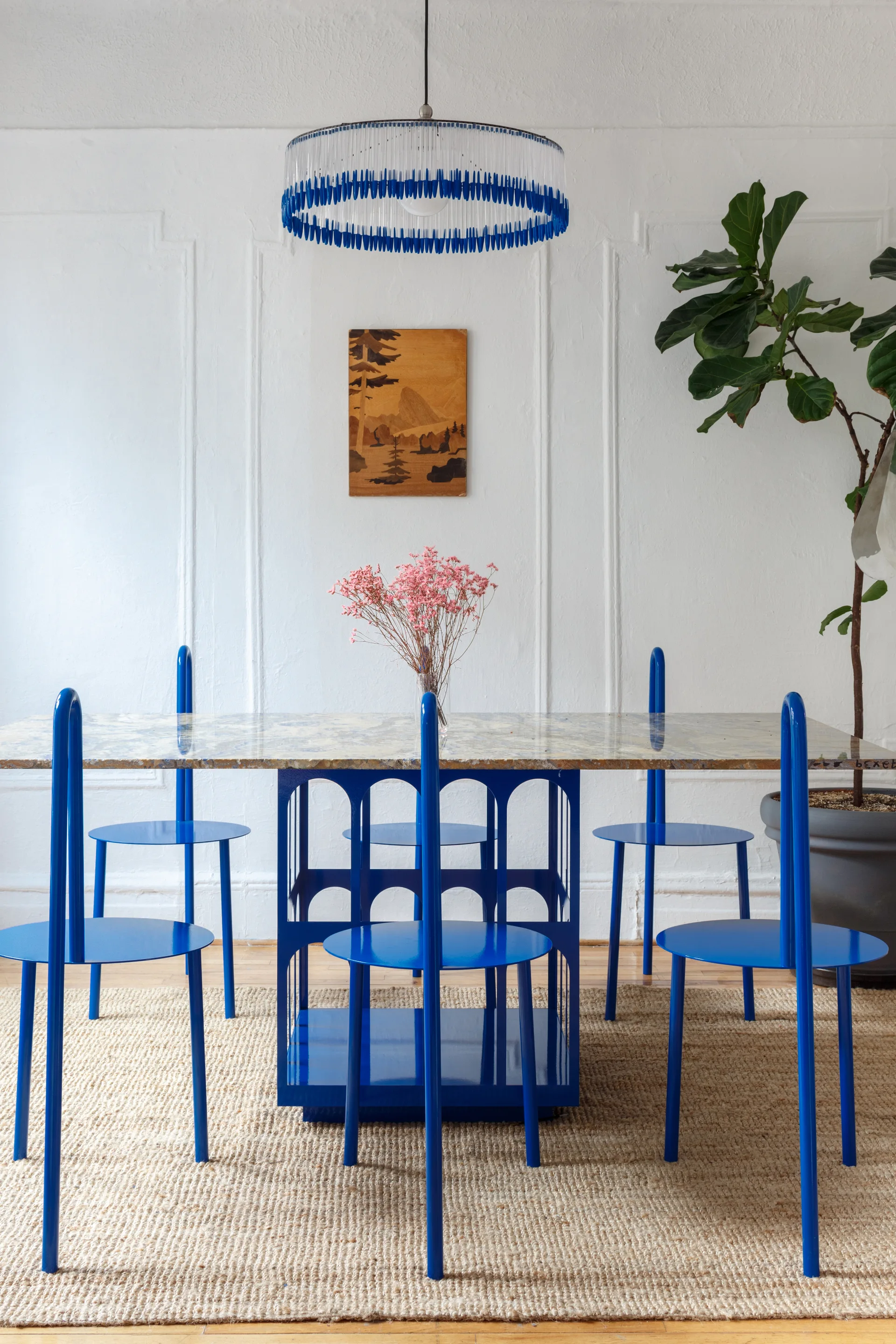 Modern dining area showing a marble table with a cobalt blue base, matching blue chairs, and a jute rug.