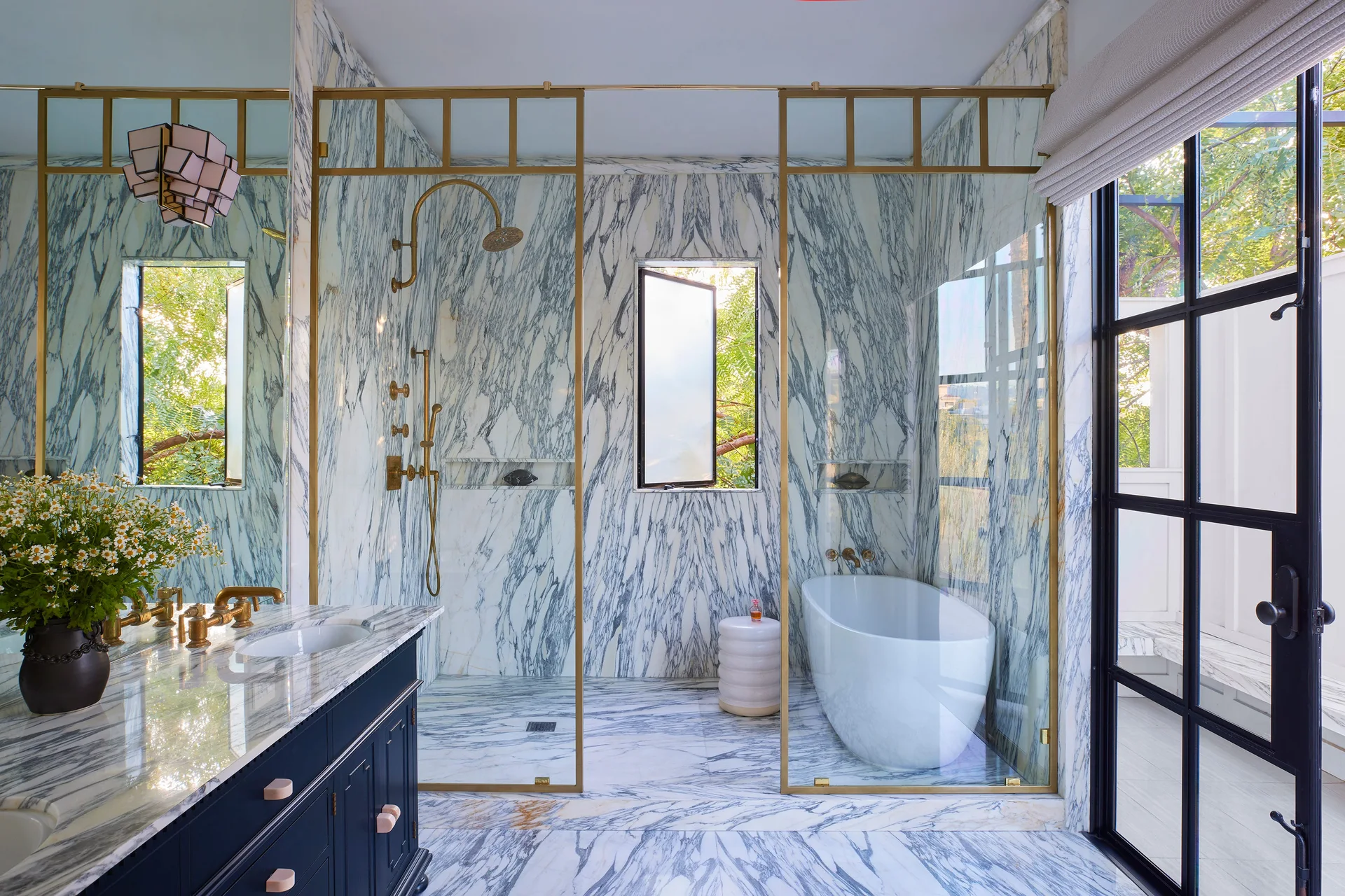A marble-clad bathroom features a navy vanity with brass hardware and a glass-enclosed wet room with a freestanding tub and shower.
