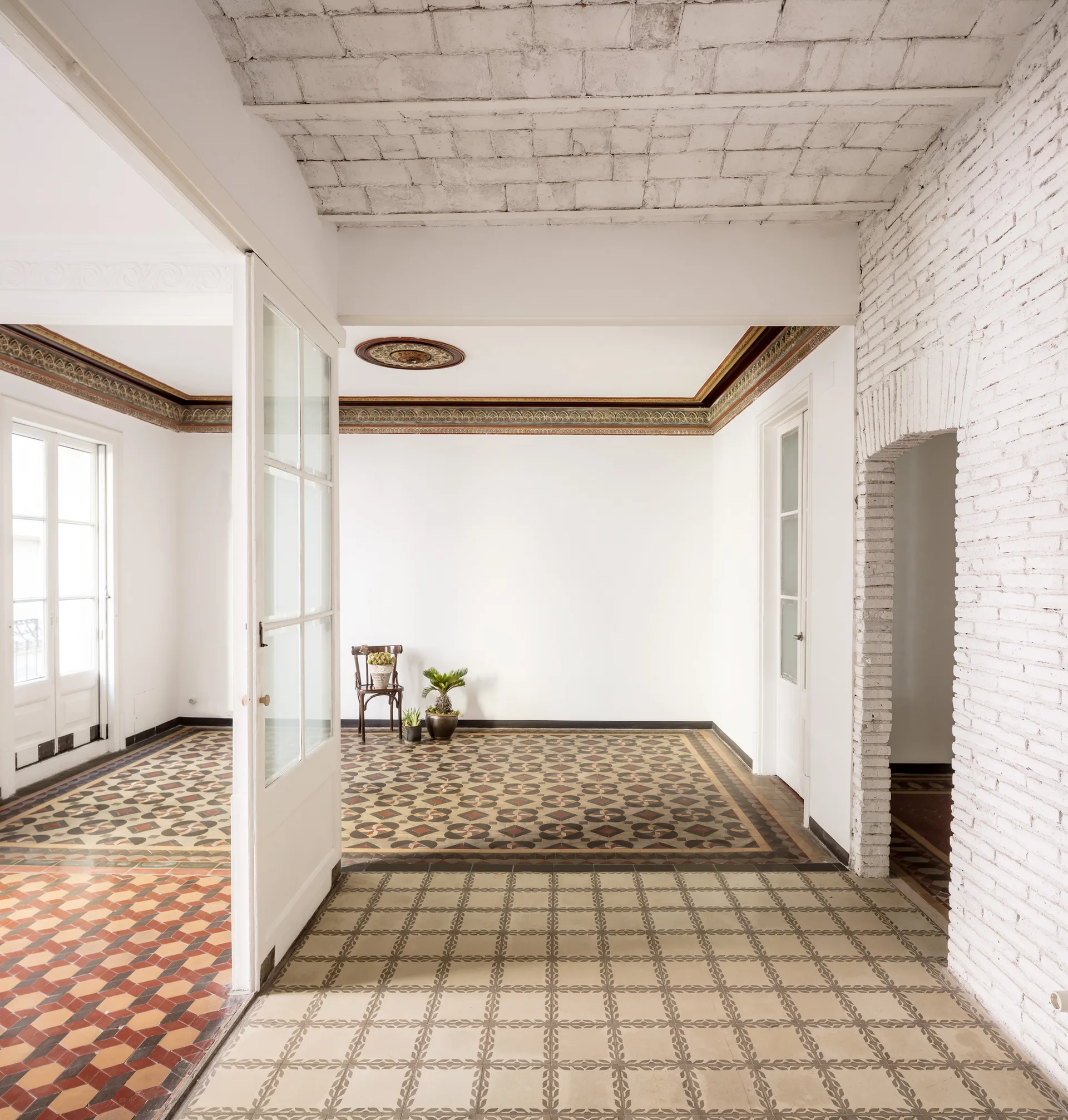 An open historic interior featuring colorful geometric tile floors, white painted brick walls, a brick ceiling, and an ornate crown molding border.