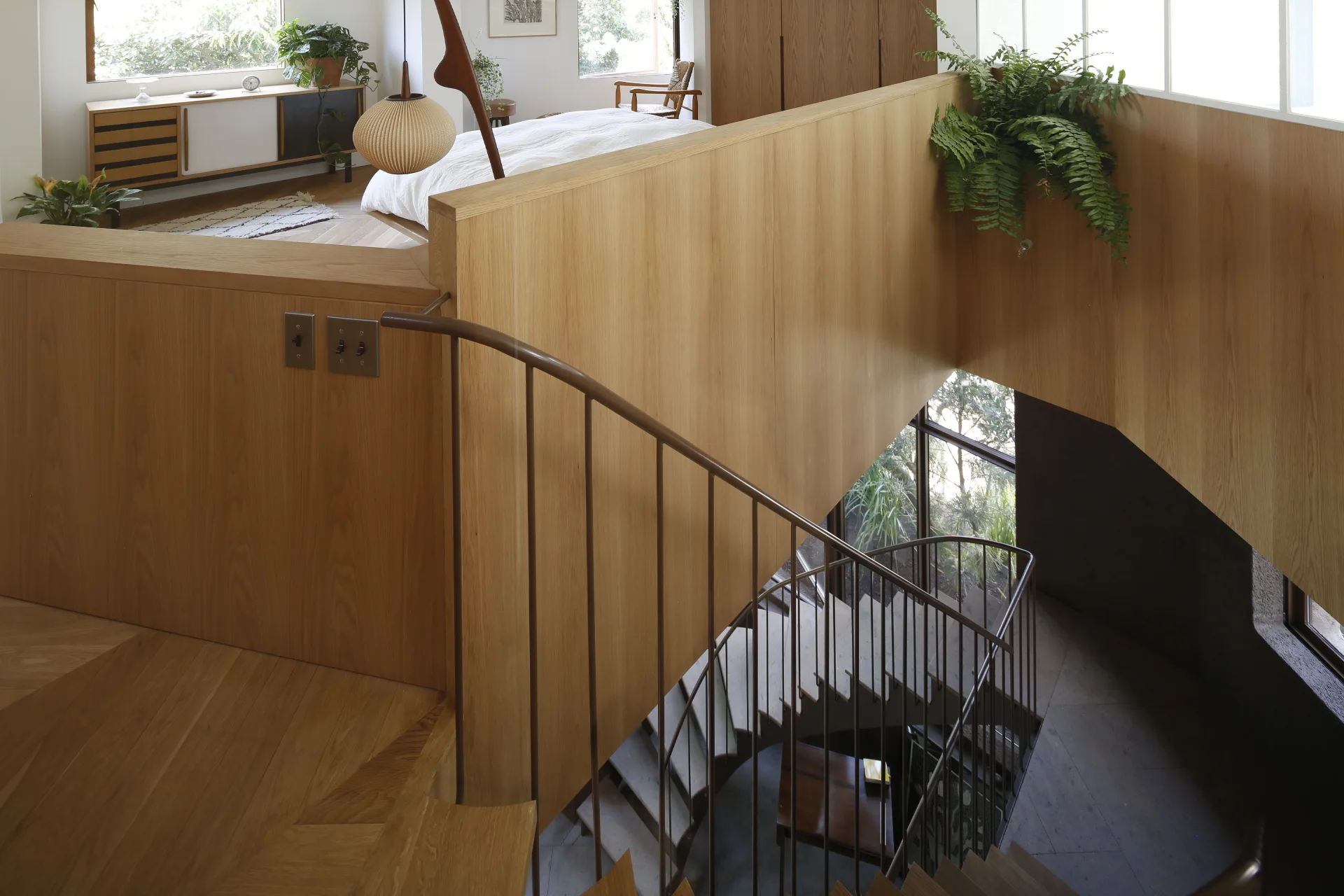 A multi-level interior view shows a curved metal staircase winding down past light wood paneled walls, with a bedroom visible on the upper level.