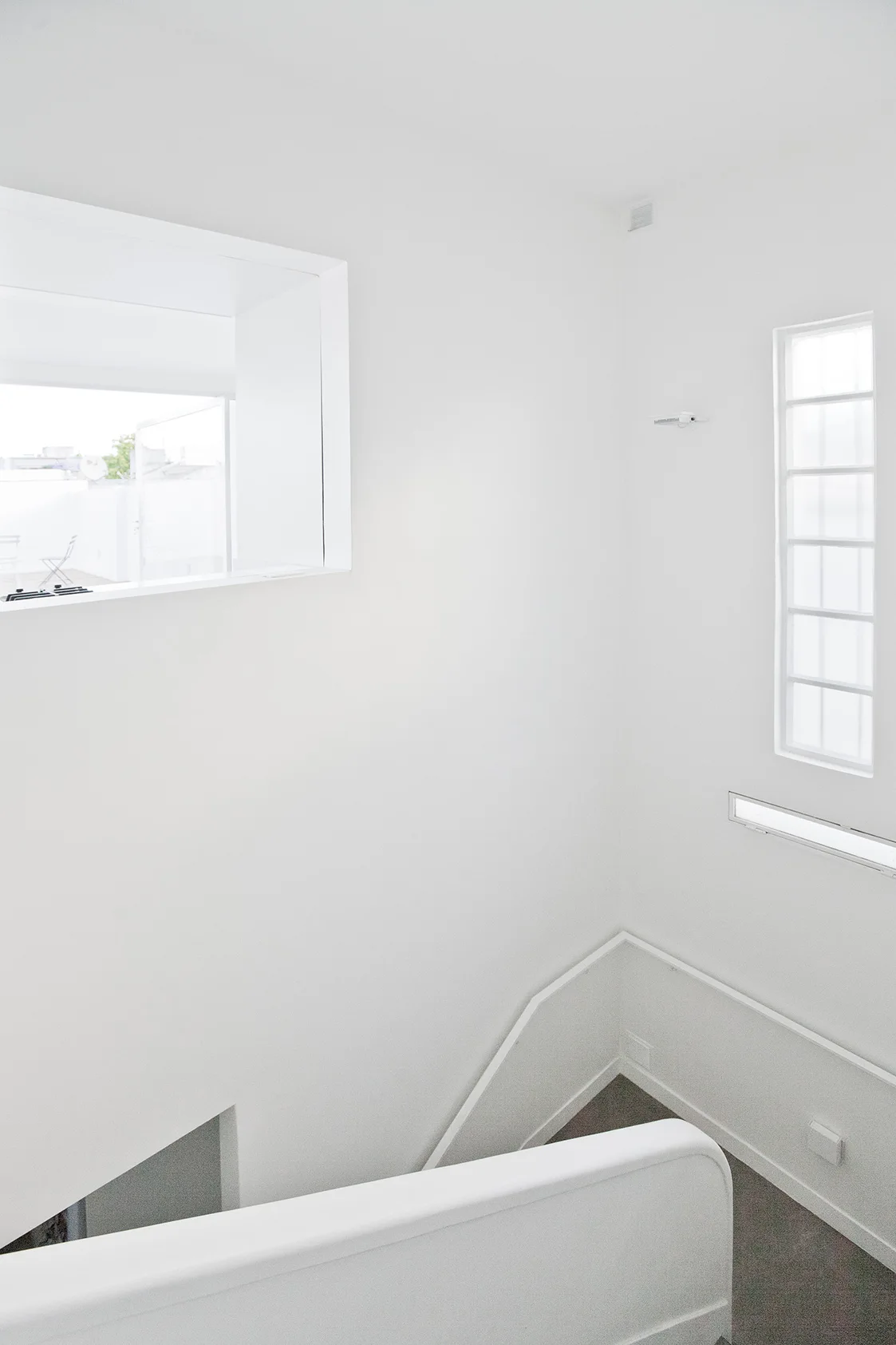 A minimalist white staircase features a curved white handrail, a large cutout window, and a vertical frosted glass block window.