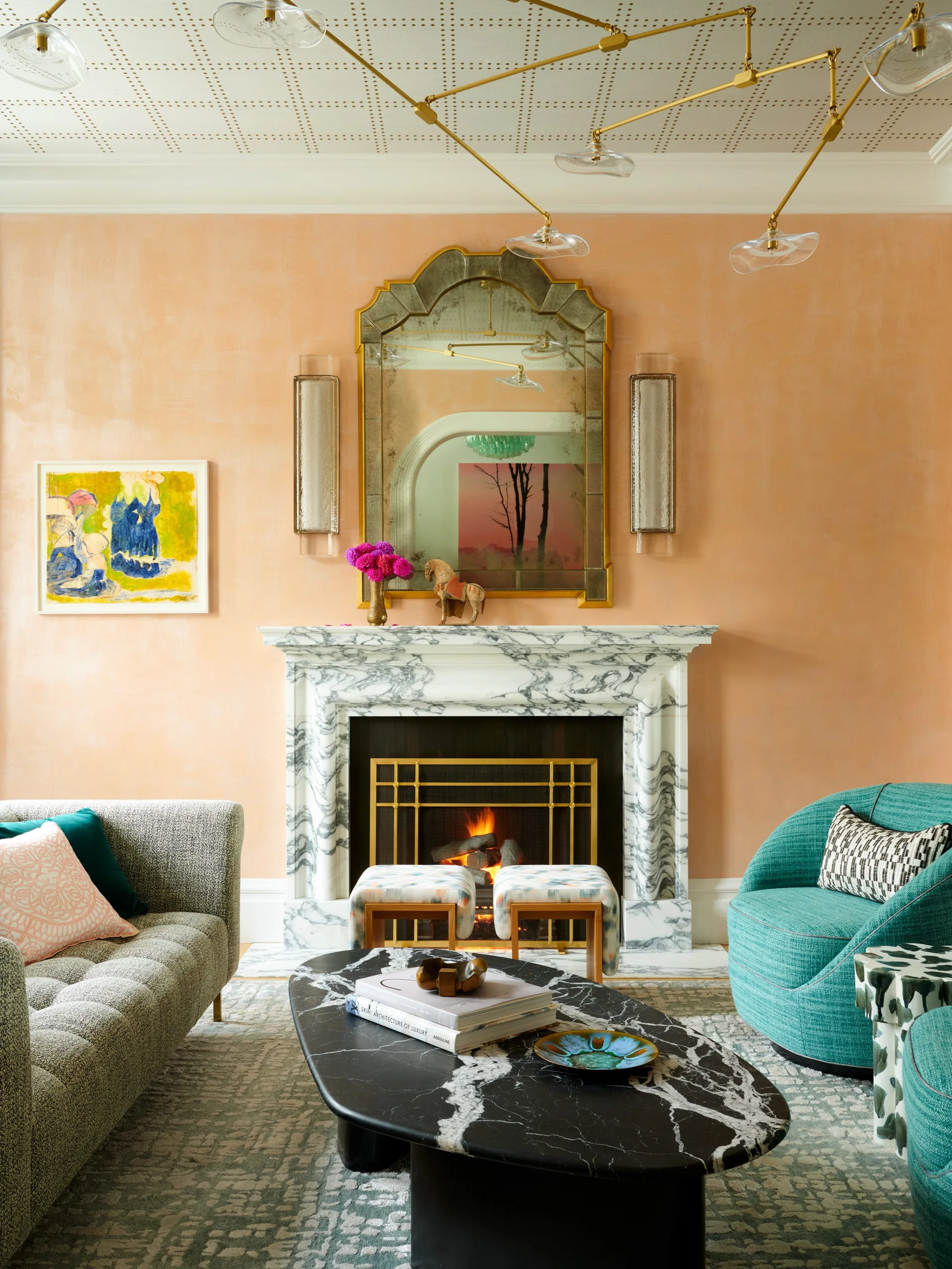 A bright living room with peach walls, a white marble fireplace, an oval black marble coffee table, and a curved teal armchair.