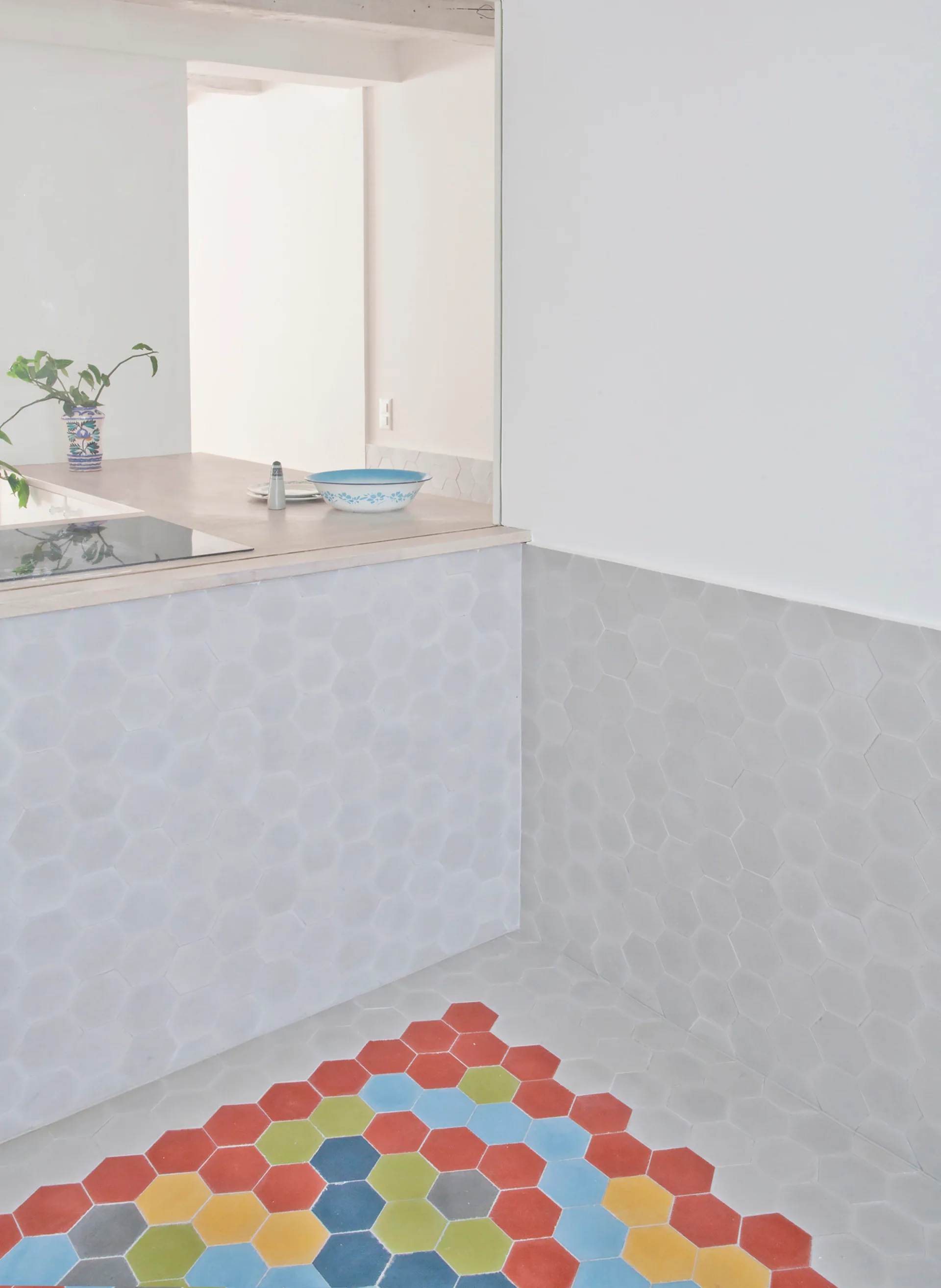 A kitchen features a light grey hexagon tiled floor and walls transitioning to a vibrant pattern of red, blue, and yellow hexagon tiles.
