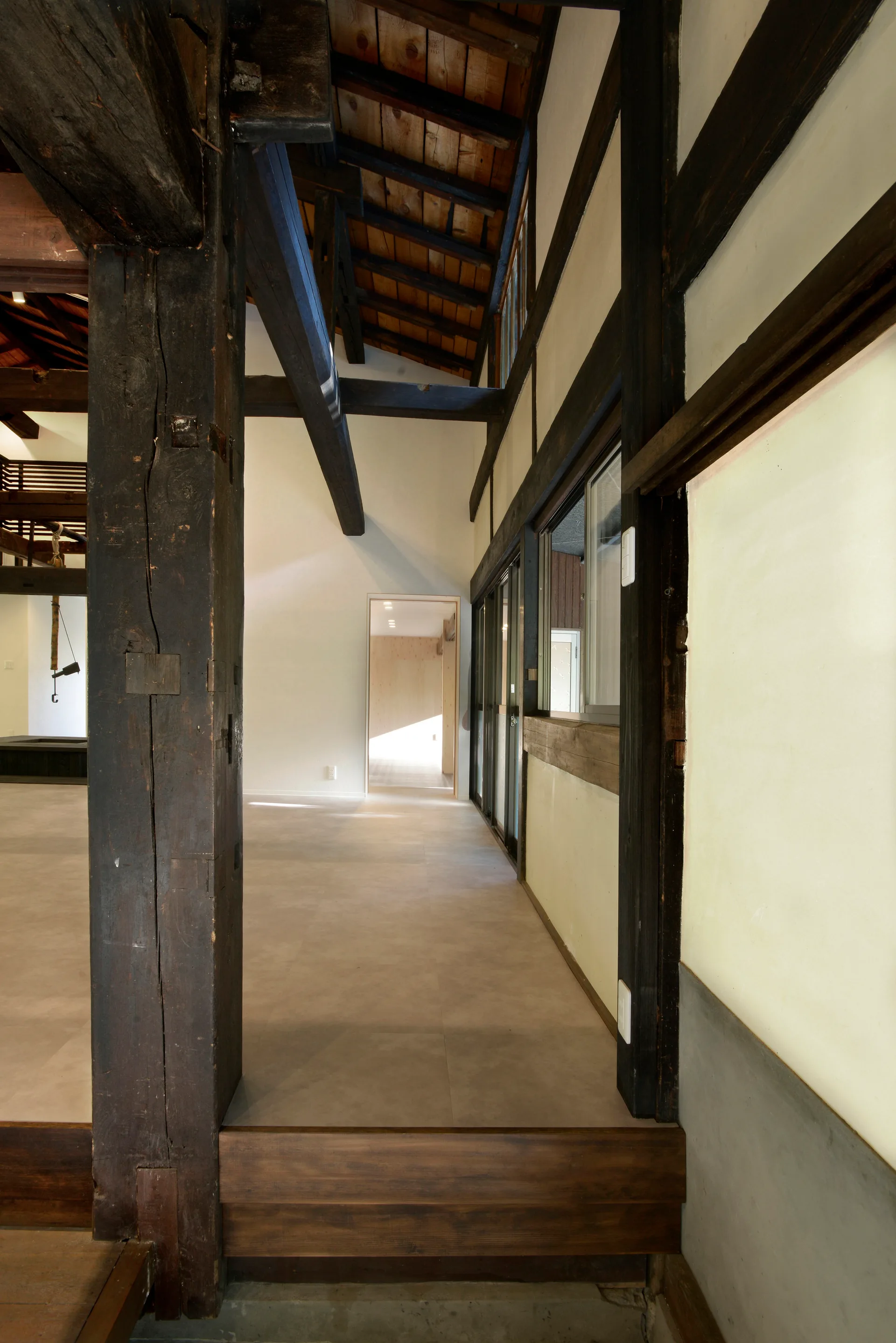 An interior hallway features large dark wood timber columns and beams set against off-white walls under a vaulted wooden ceiling.