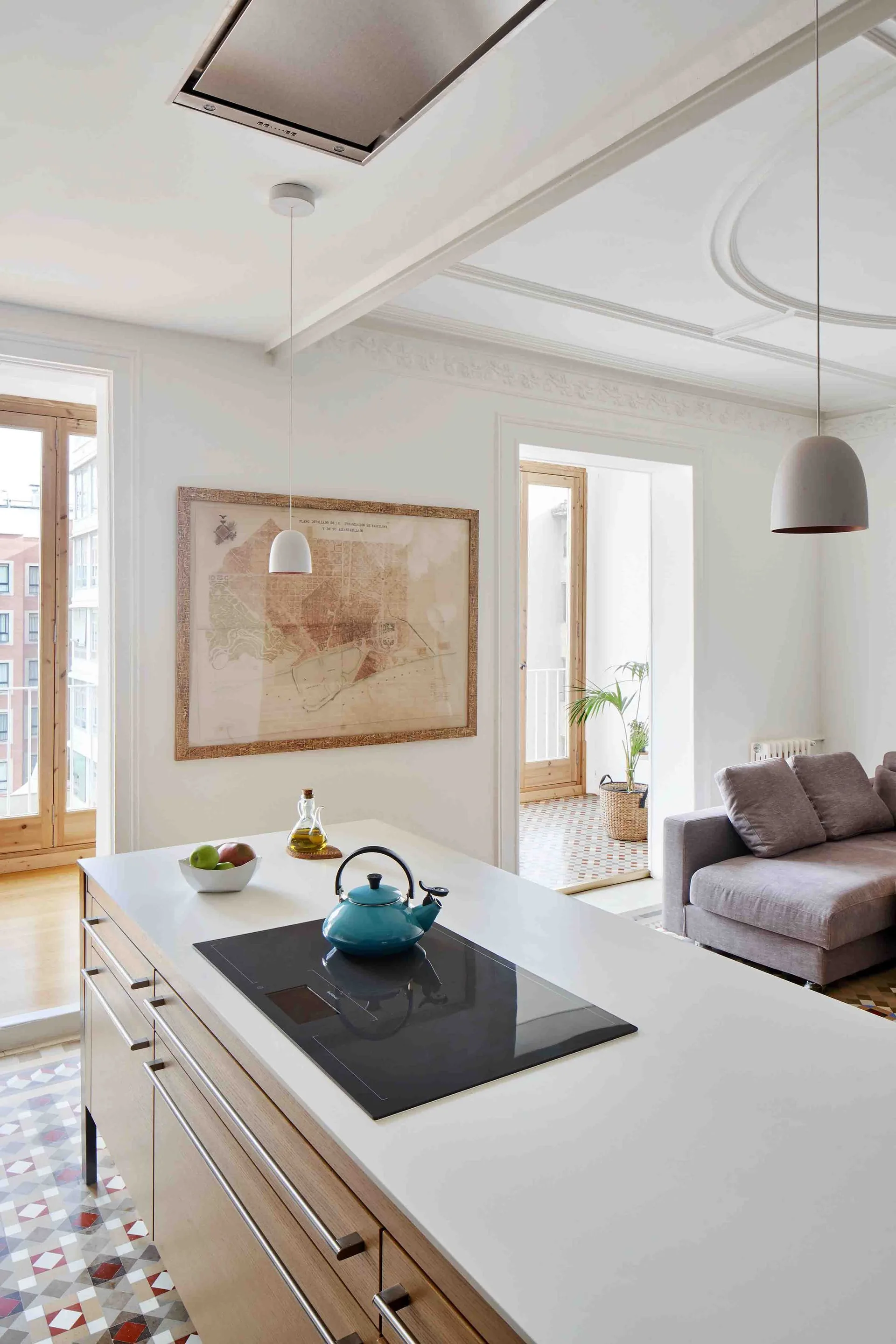 A light-filled kitchen featuring a modern wood island with a white countertop, patterned tile floors, and decorative white ceiling moldings.