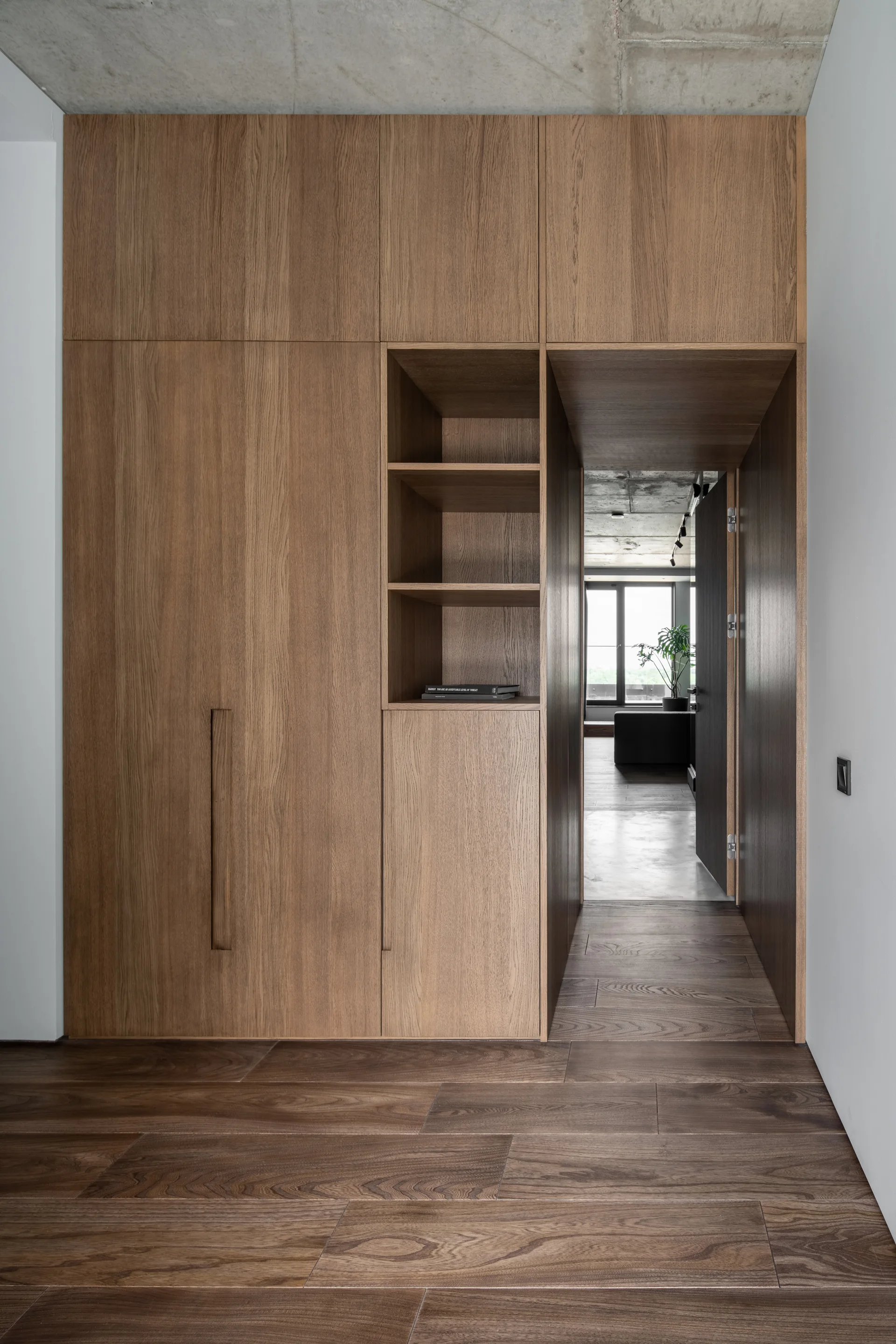 Floor-to-ceiling wood cabinetry with an integrated doorway, built-in shelving, and wood flooring under an exposed concrete ceiling.
