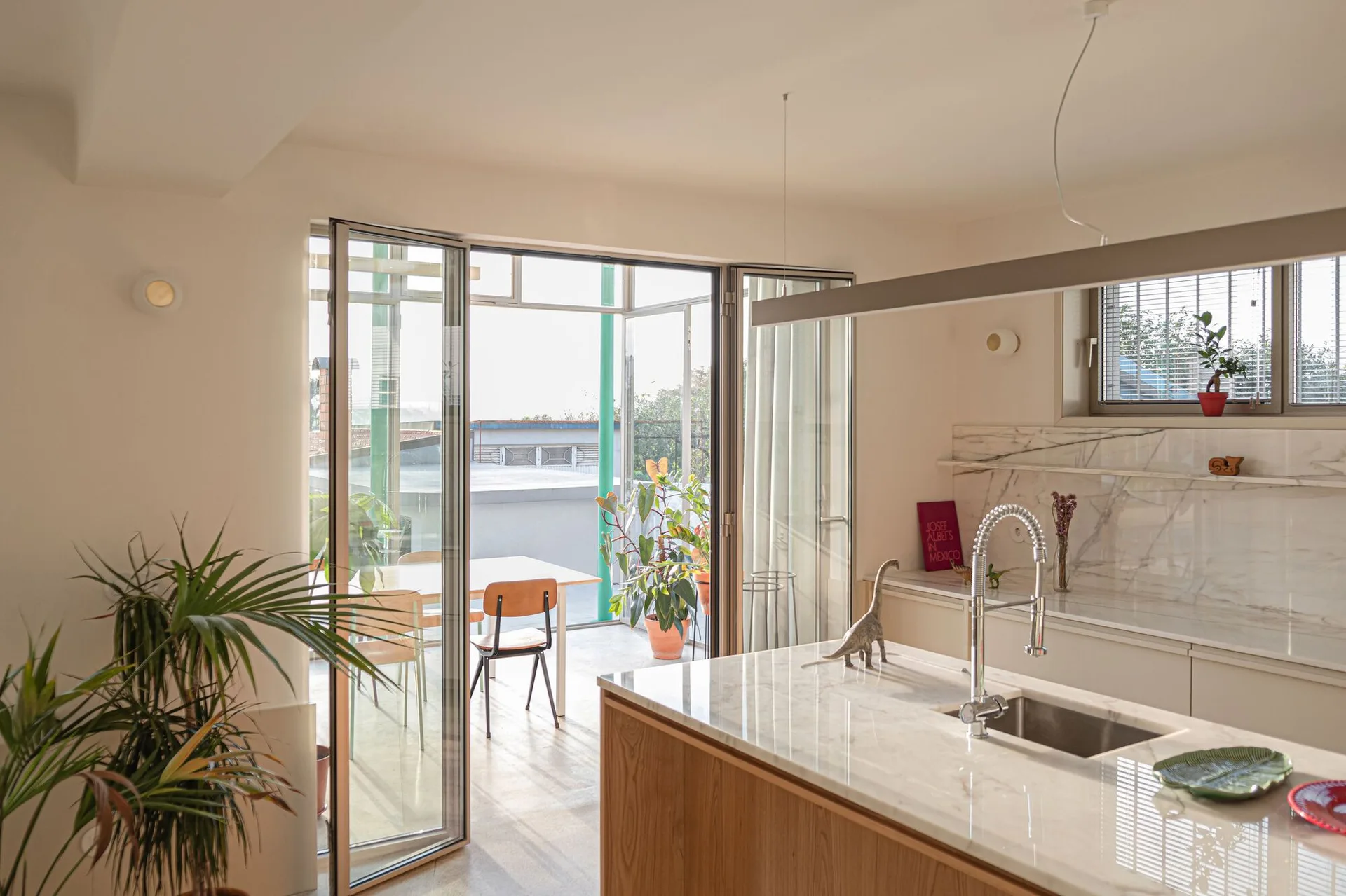 A bright kitchen features a marble-topped wood island and a matching marble backsplash with folding glass doors that open to an outdoor dining terrace.