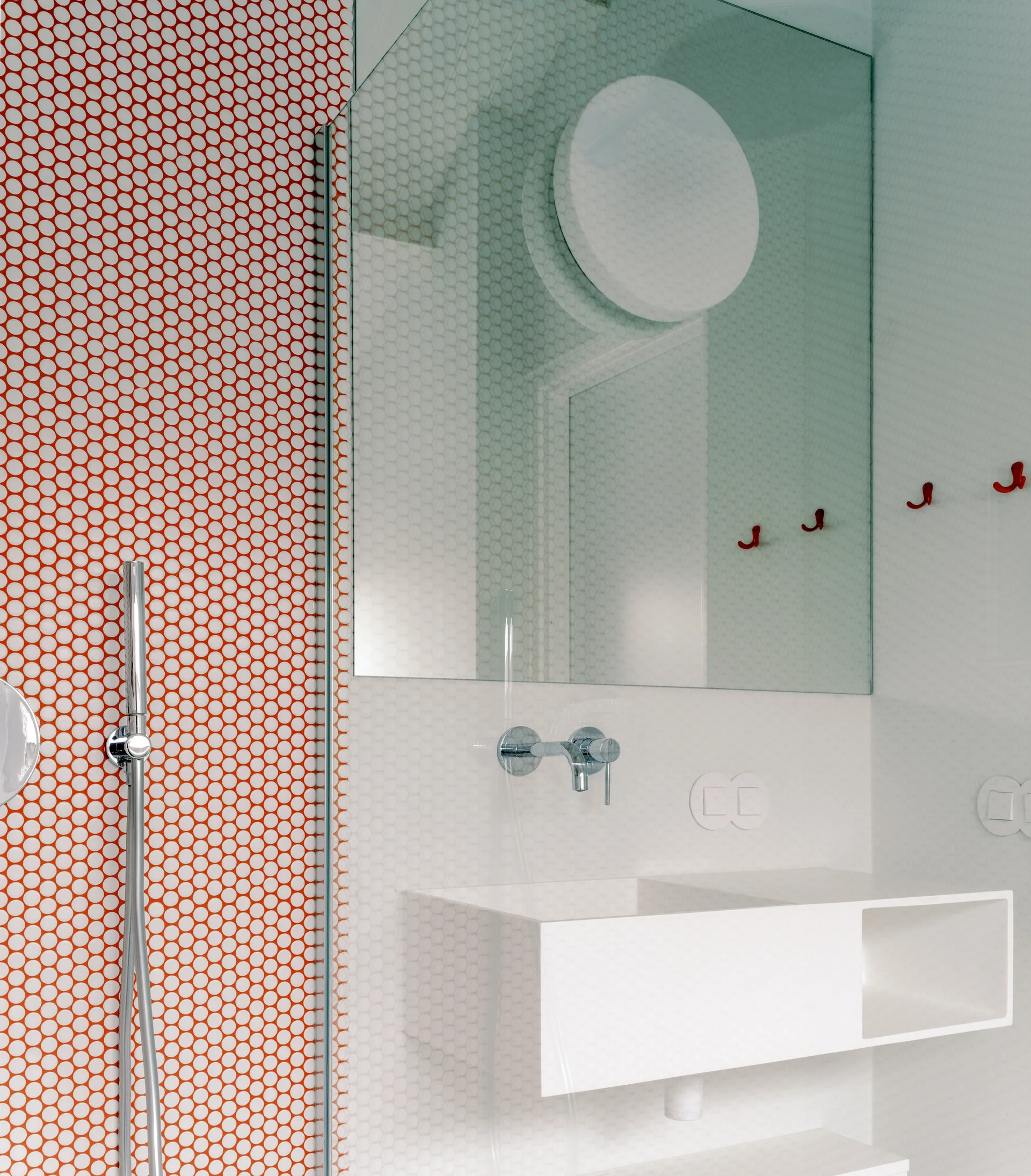 A modern bathroom features a bright orange penny tile wall in the shower, a white wall-mounted sink with chrome faucet, and a large mirror.