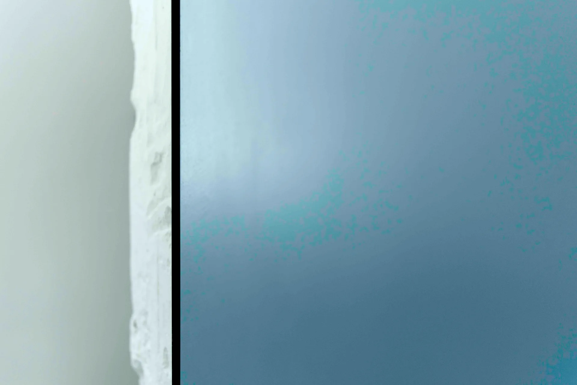 A close-up view of a rough textured white plaster wall meeting a smooth matte grey-blue painted surface with a sharp vertical edge.