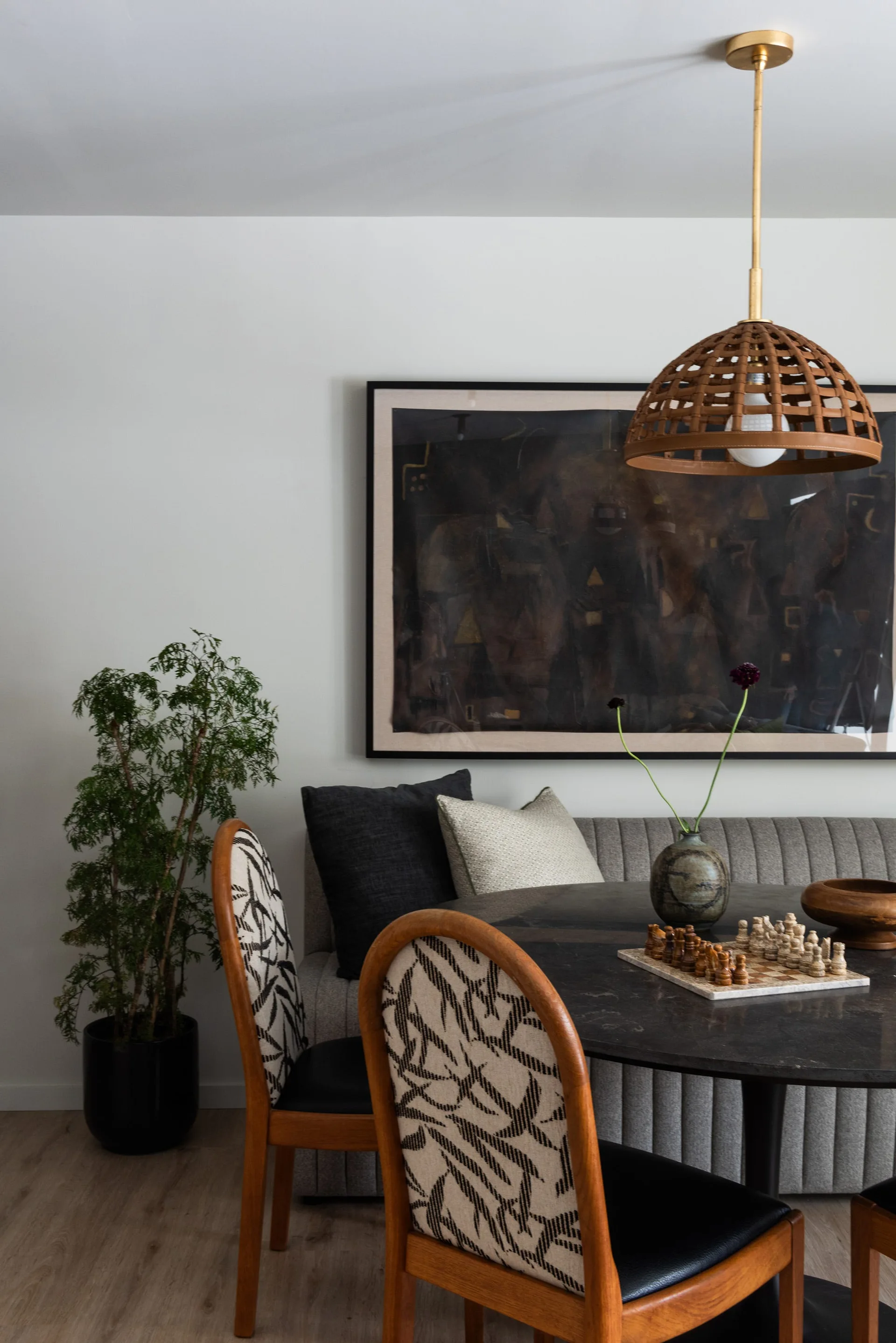 A modern dining nook featuring a circular dark stone table, a gray channel-tufted banquette, and wooden chairs with graphic black and white upholstery.