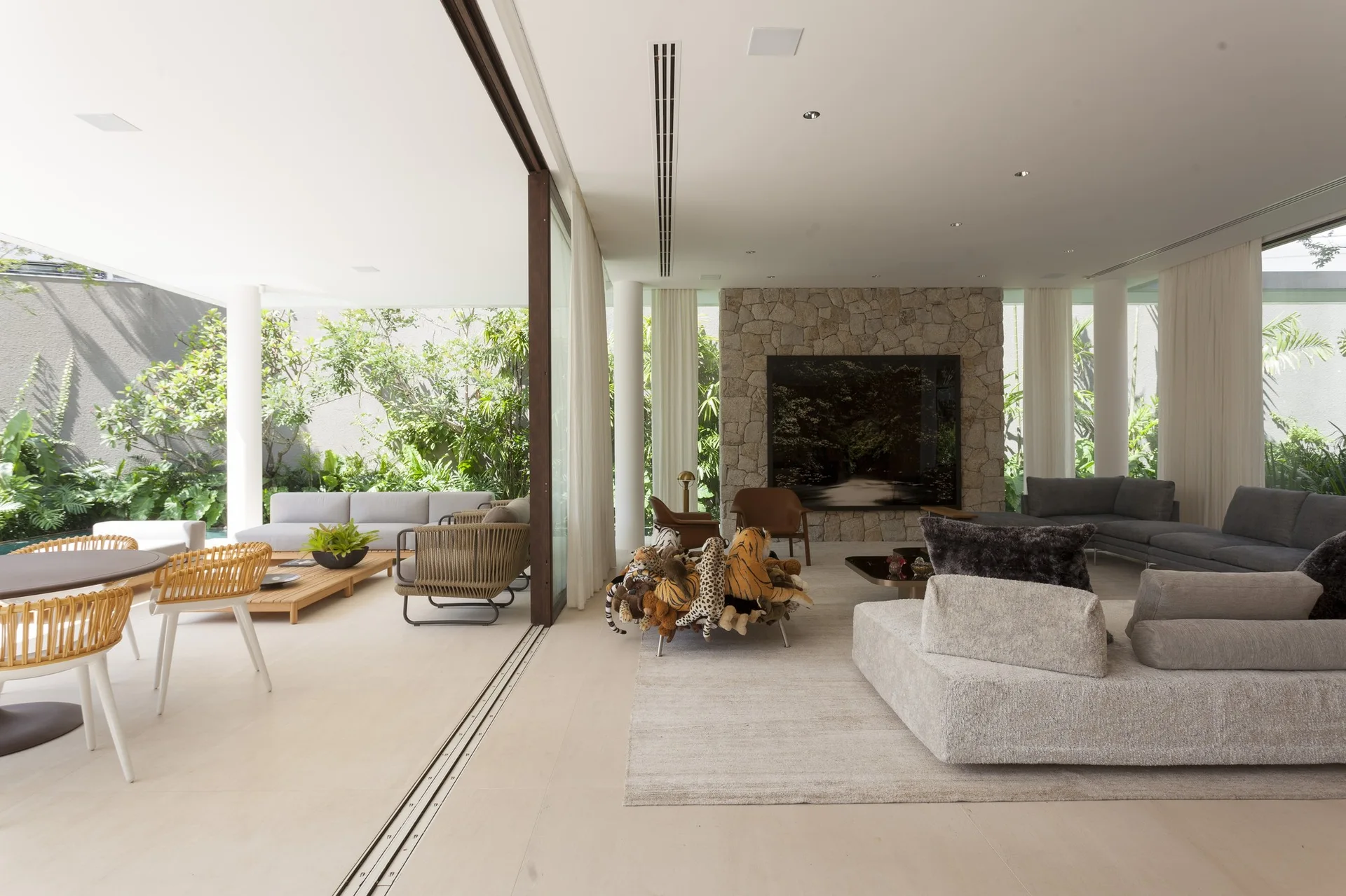 A spacious contemporary living room with a large stone feature wall transitions through open sliding glass doors to a furnished patio.