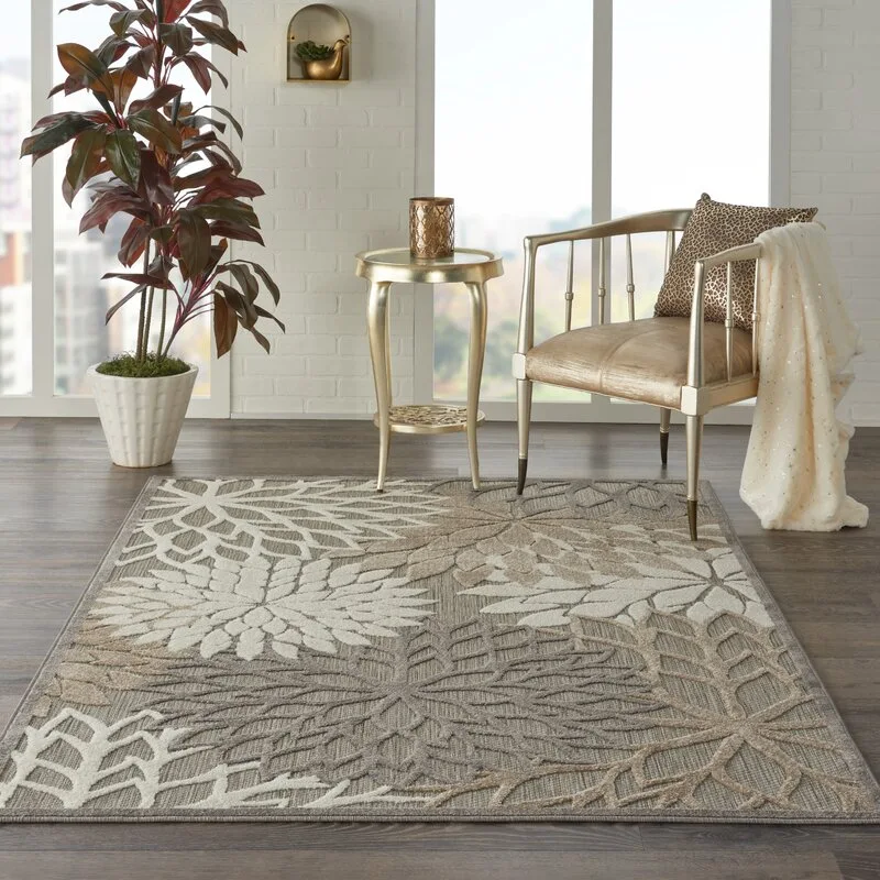 A neutral-toned floral area rug on a dark wood floor near a gold metallic armchair and side table in front of a white brick wall.