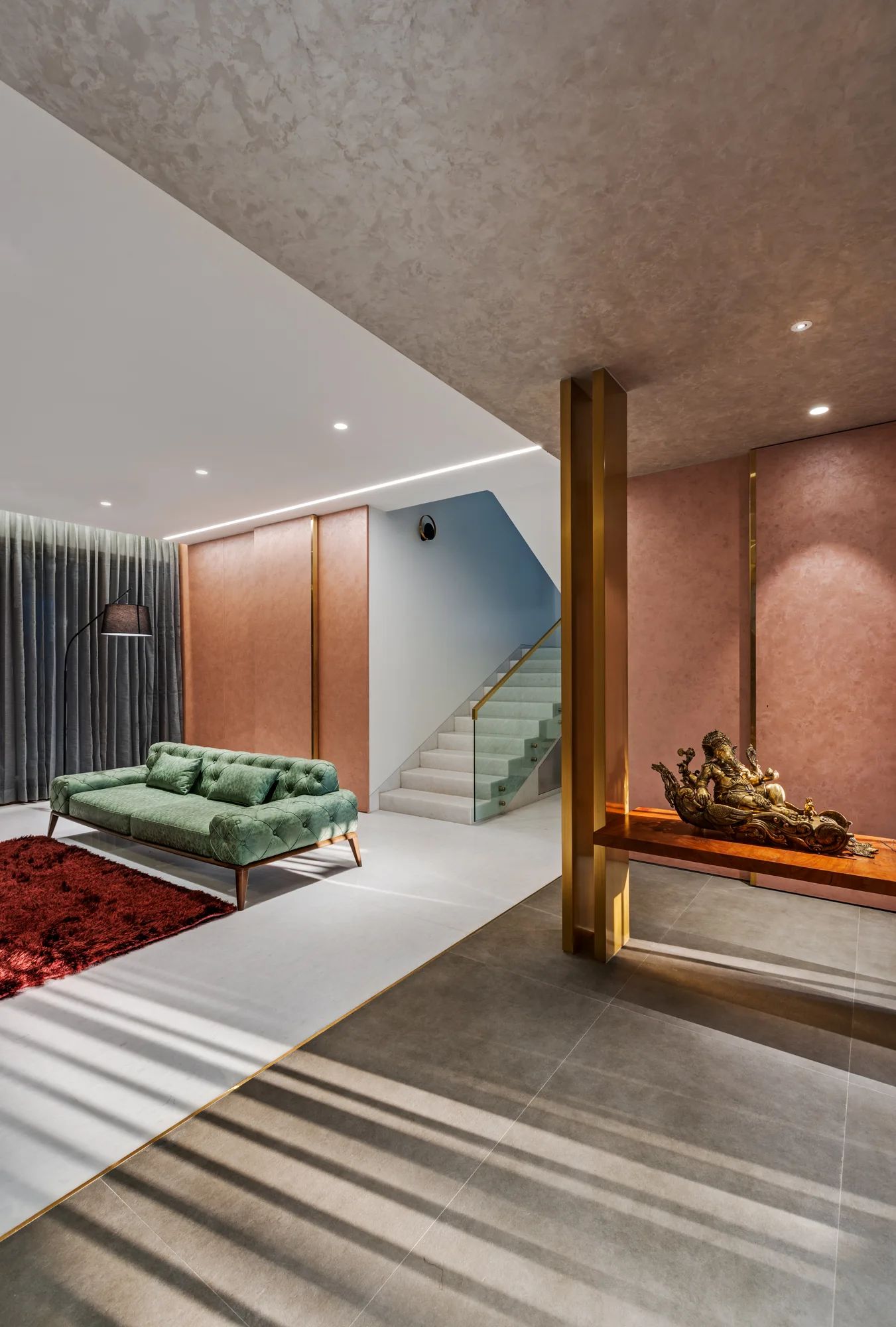 A contemporary living space features a tufted green sofa, textured rose wall paneling, a wooden console table, and a modern staircase in the background.