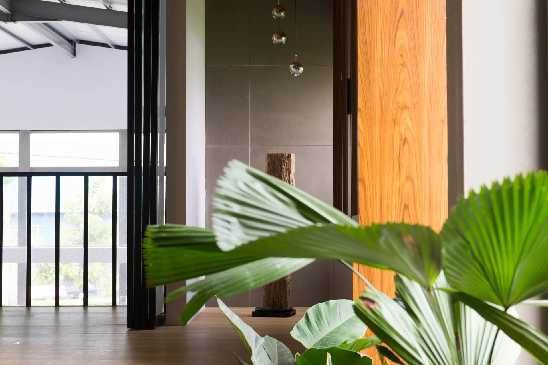 A modern minimalist hallway with grey wall panels, a tall wood log sculpture, and a large green plant in the foreground.
