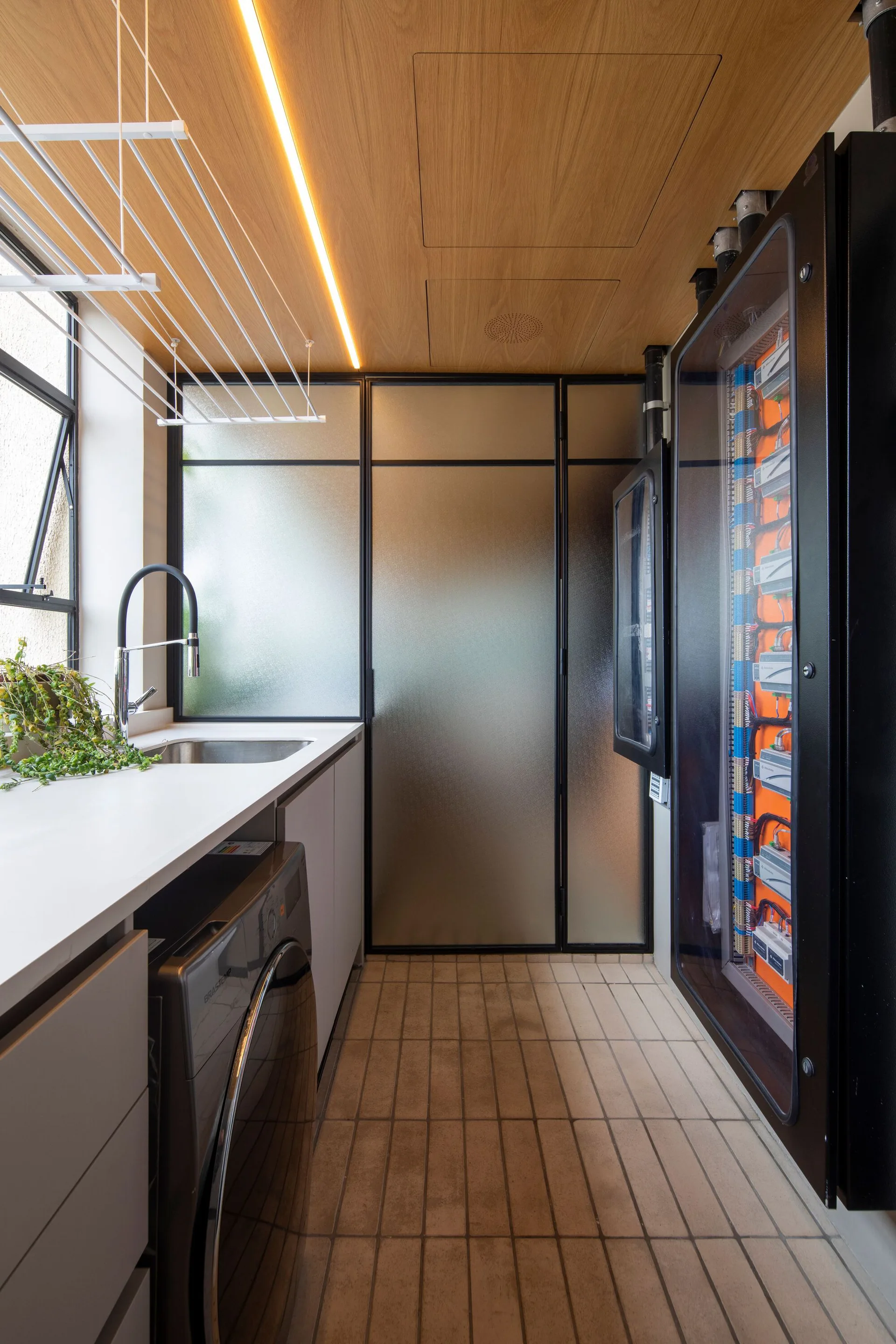 A narrow laundry room with a light wood ceiling, integrated washing machine, ceiling-mounted drying rack, and frosted glass partition.