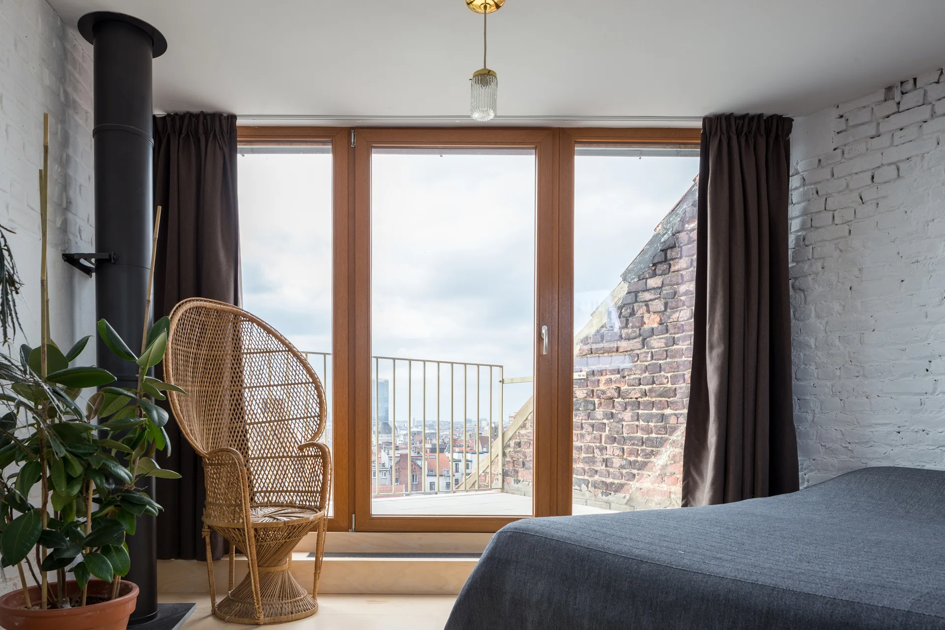 A loft bedroom featuring a woven rattan peacock chair beside large wood-framed glass doors that open to an outdoor balcony.