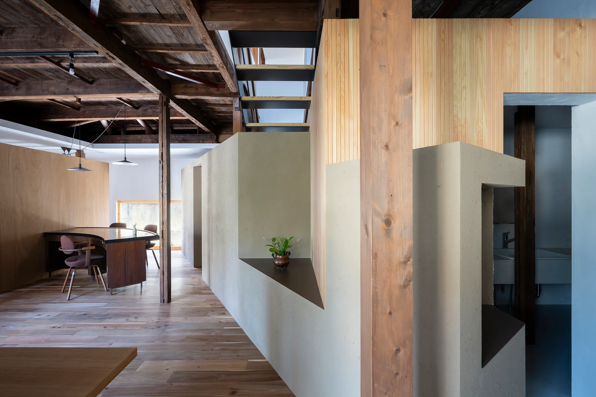 A modern interior space showcases a textured beige plaster partition wall with a small shelf cutout beneath exposed dark wood ceiling beams.