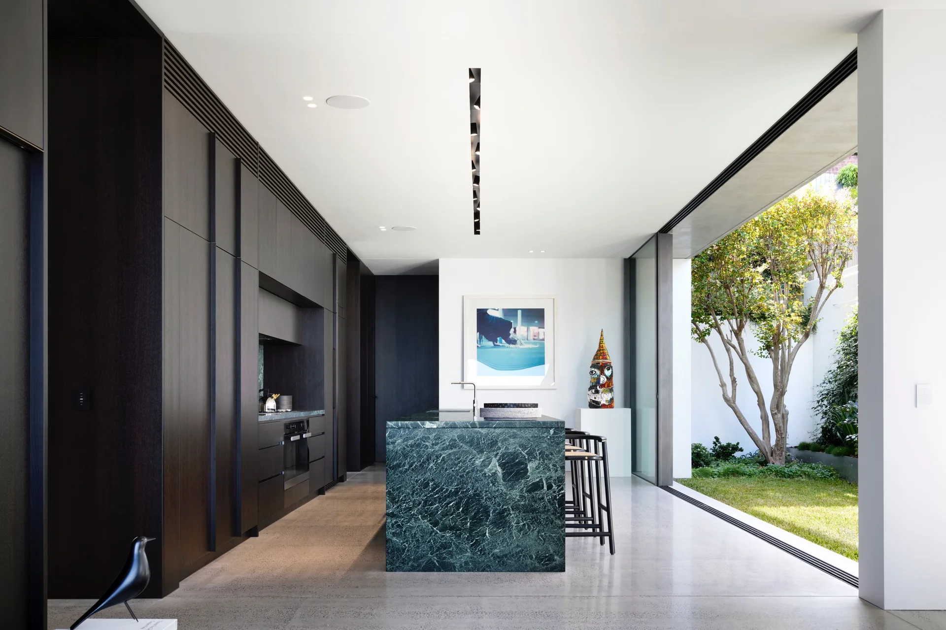 A modern kitchen features a green marble island, dark wood cabinetry, and a sliding glass door leading to a garden.