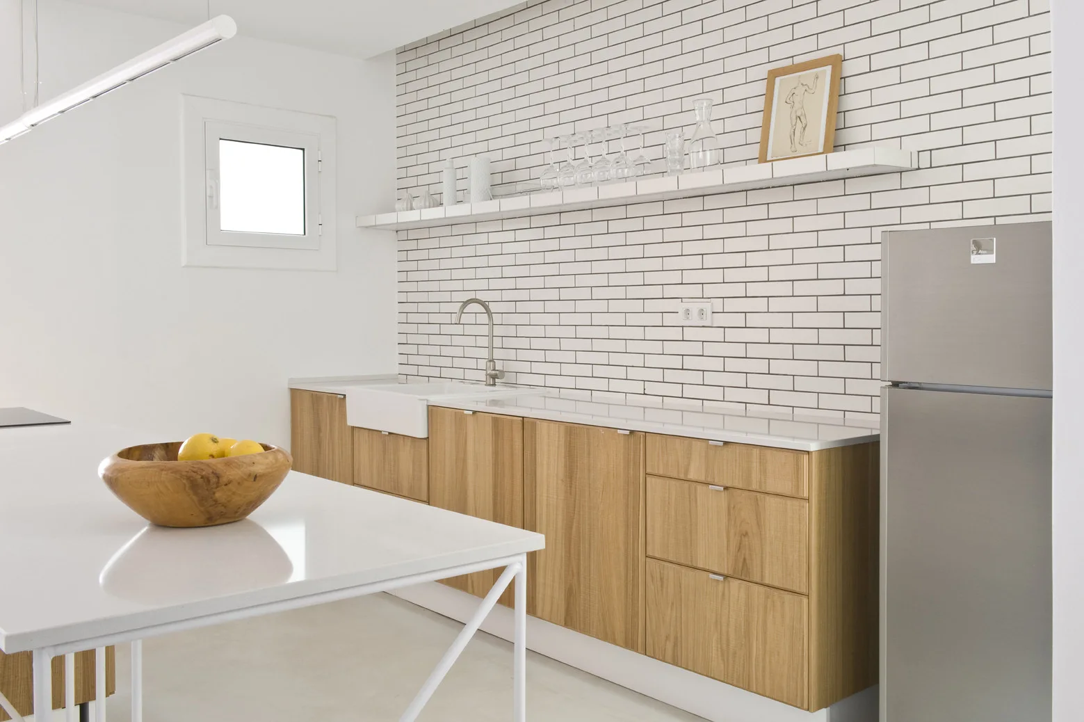 A bright kitchen featuring a white subway tile wall, natural wood base cabinets, an apron-front sink, and a white kitchen island.