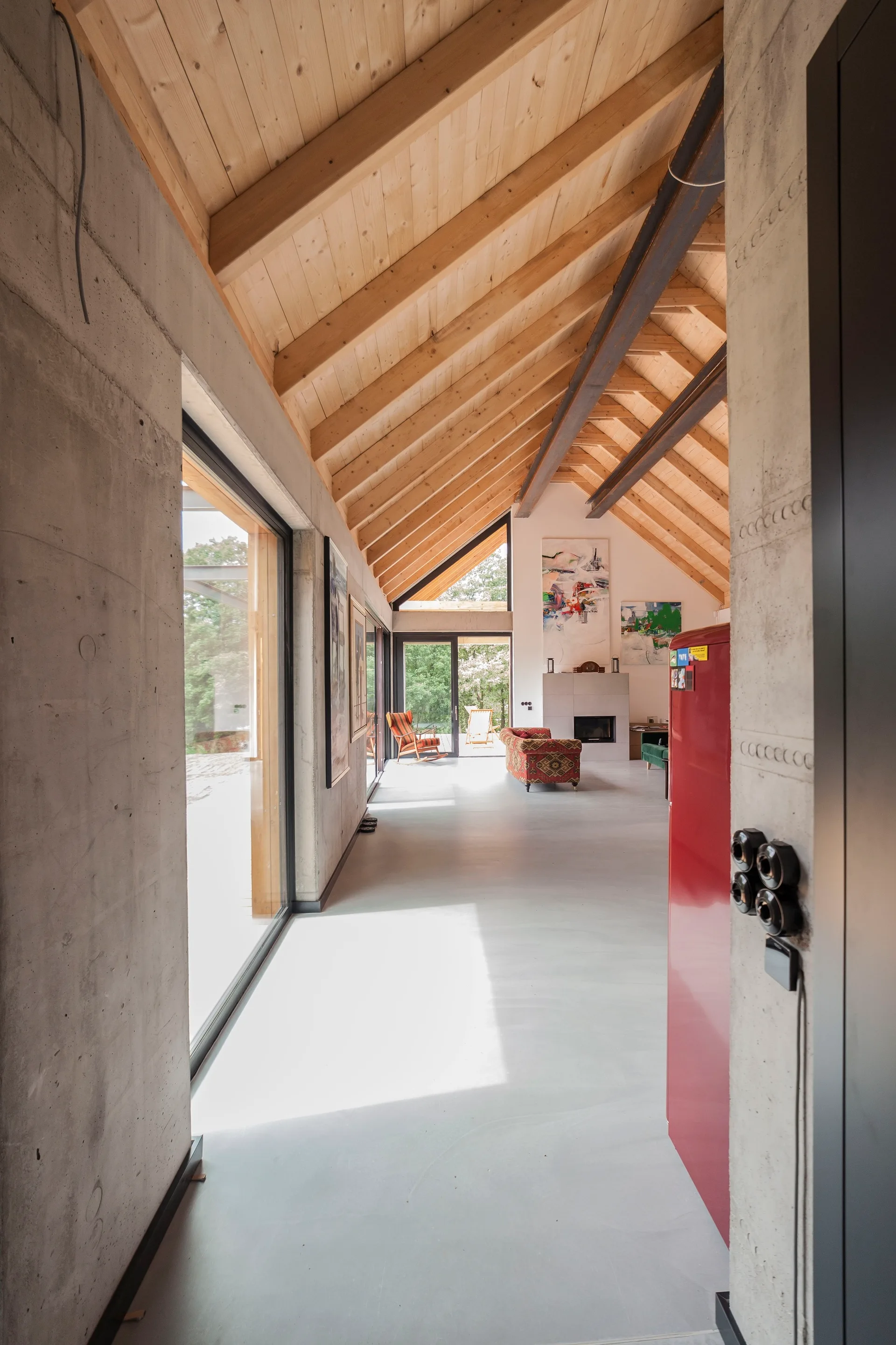 An open living space with a high vaulted ceiling made of exposed wooden rafters, raw concrete walls, and large sliding glass doors.