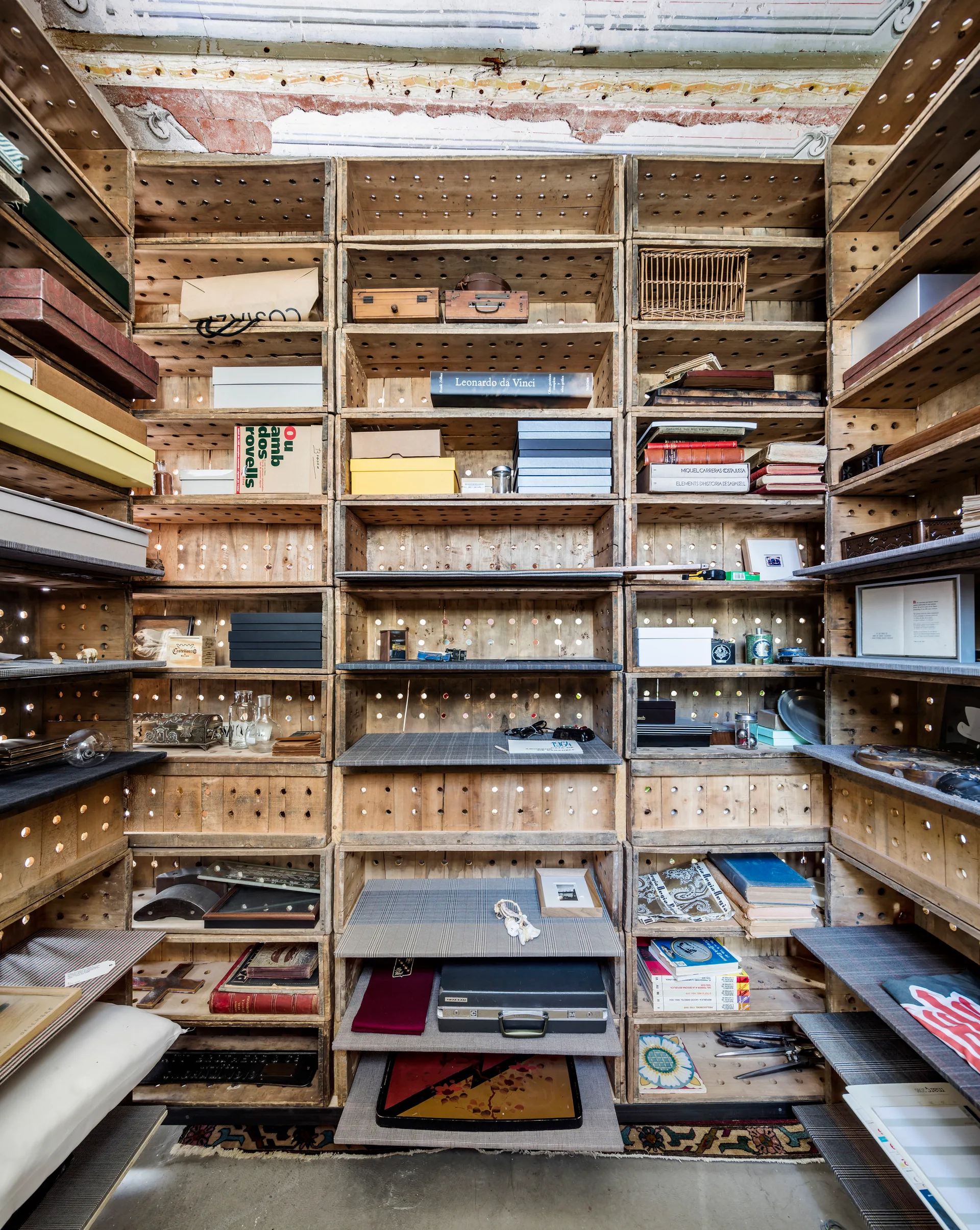 A floor-to-ceiling storage unit built from stacked wooden crates holding books, boxes, and decorative objects.