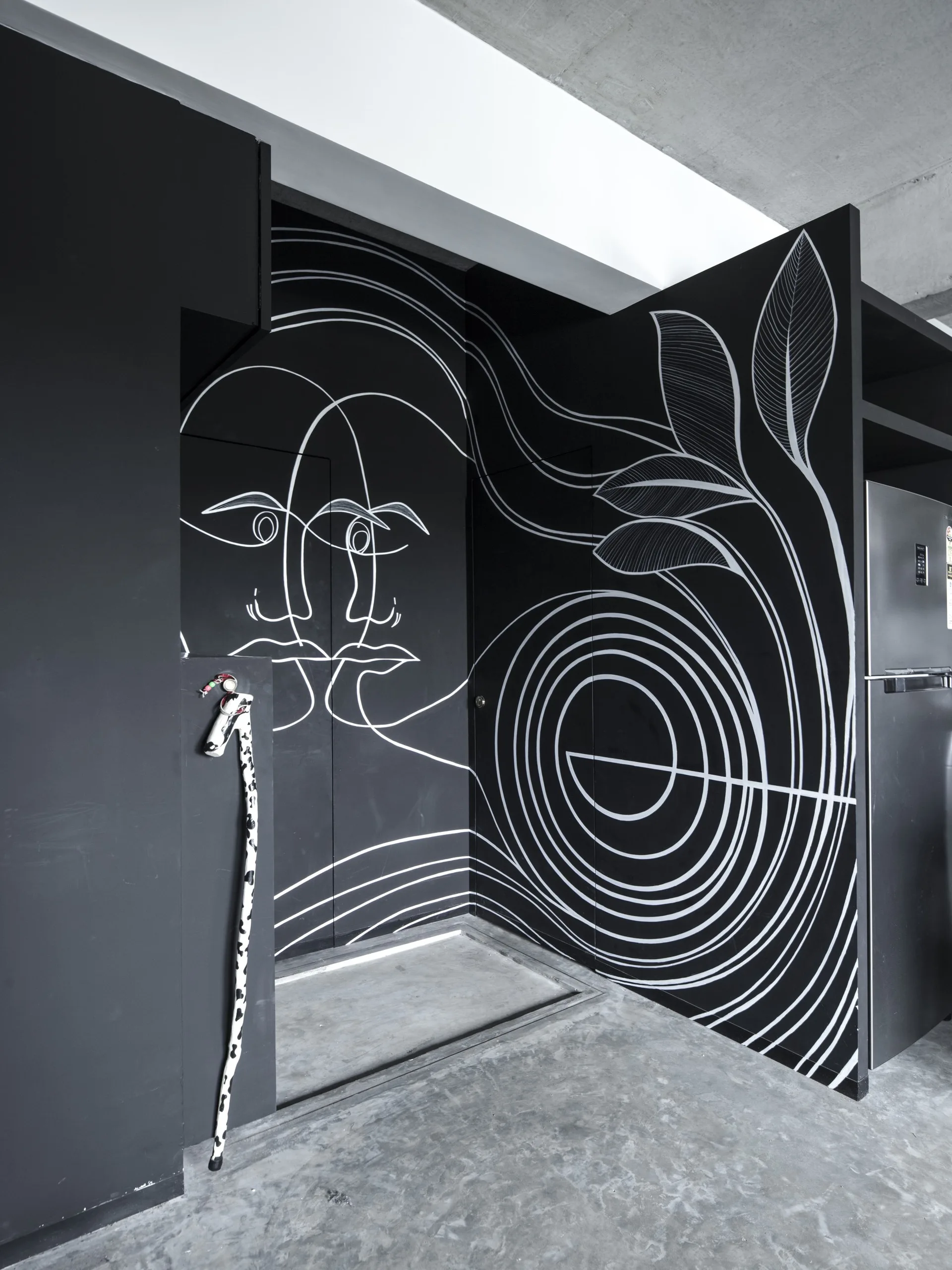 A matte black interior wall features a large white line-art mural depicting abstract faces and leaf designs next to a concrete floor.